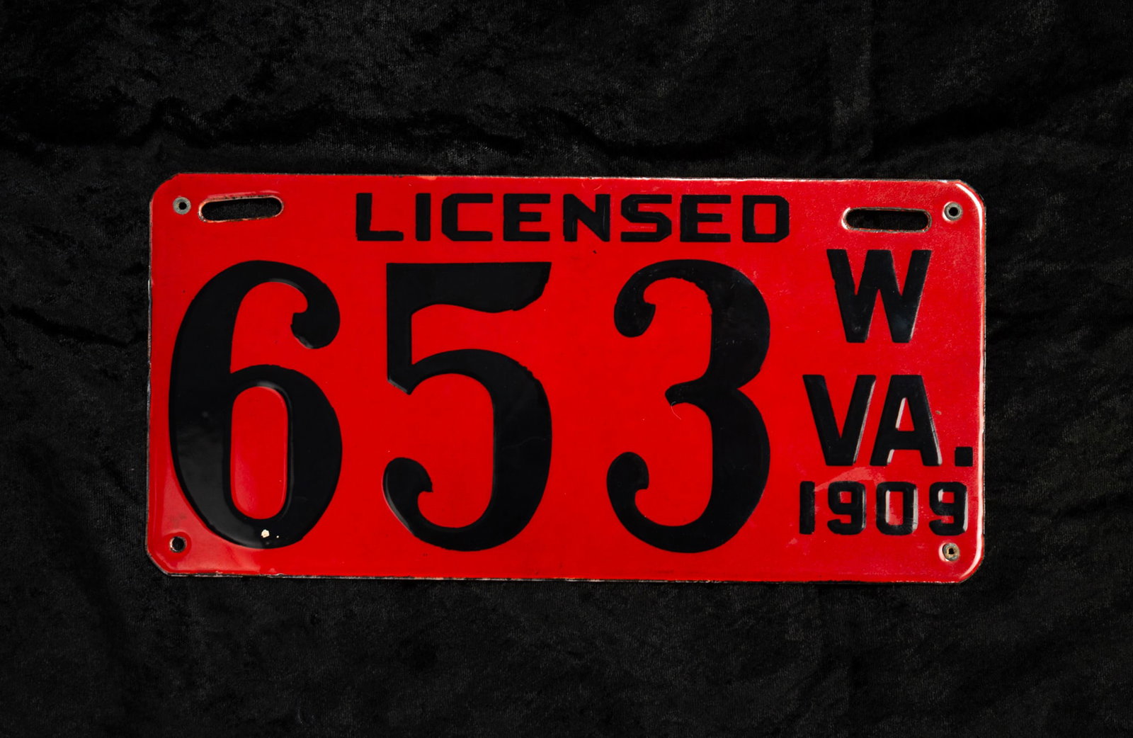 WEST VIRGINIA 1909 LICENSE PLATE MANUFACTURE BY THE BALTIMORE ENAMEL AND NOVELTY COMPANY.: WEST VIRGINIA 1909 LICENSE PLATE MANUFACTURE BY THE BALTIMORE ENAMEL AND NOVELTY COMPANY. American. Iron with red enameled front, black lettering "LICENSED W VA. 1909" and license number "653". White