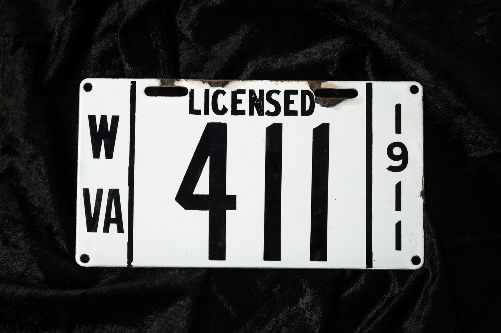 WEST VIRGINIA 1911 ENAMELED LICENSE PLATE.: WEST VIRGINIA 1911 ENAMELED LICENSE PLATE. American. Iron with white enamel and black lettering "W VA LICENSED 1911" and license number "411". 5.5"h. 10"w. Provenance: From the late George Shahady (Br