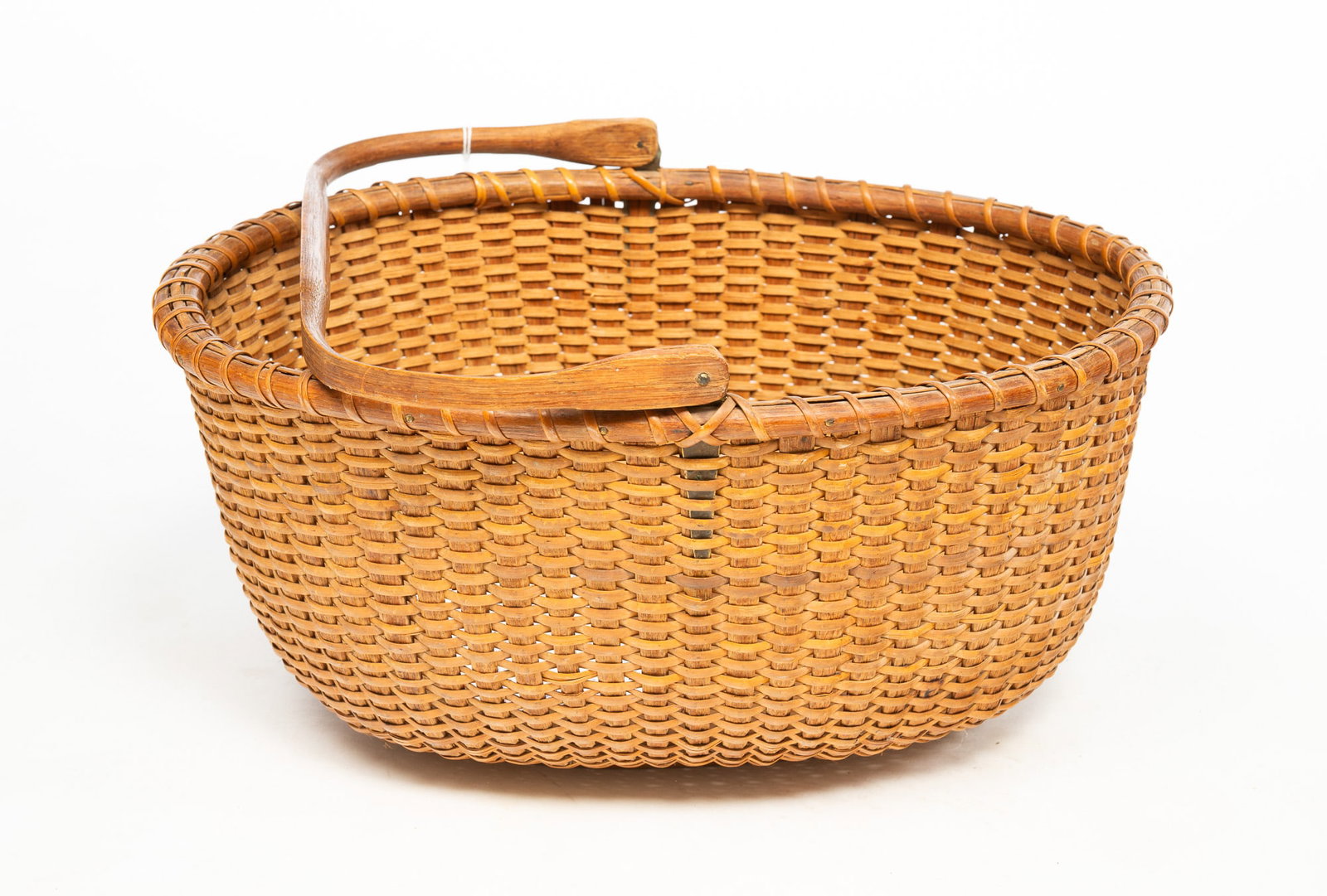 OVAL NANTUCKET SWING HANDLE BASKET.: OVAL NANTUCKET SWING HANDLE BASKET. American, 19th Century. Oval woven cane with wooden base basket and a bentwood swing handle. 7.5"h. 16.5"w. Provenance: The Lifetime Collection of the late Nancy