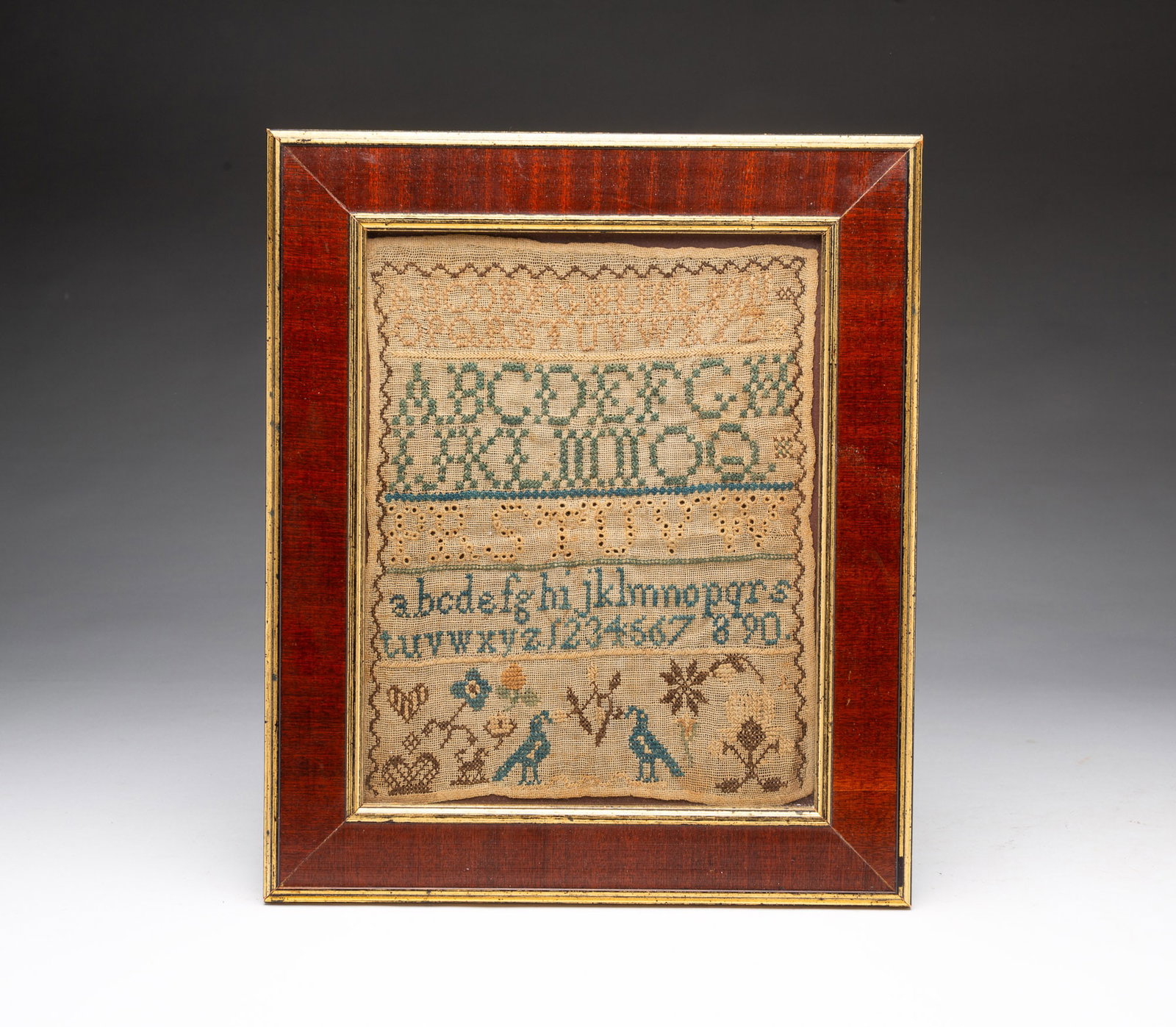 NEEDLEWORK SAMPLER WITH BIRDS.: NEEDLEWORK SAMPLER WITH BIRDS. English, 19th Century. Colored thread on linen. Rows of alphabets and numerals in various stitches, above a tableau of a crown, heart, flowers, and birds. Sight, 9.5"h.