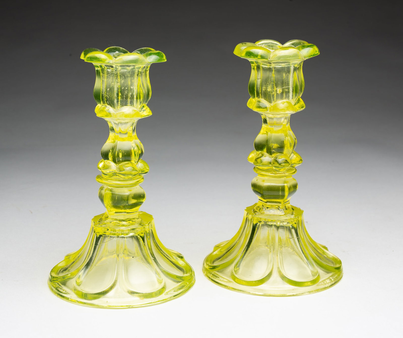 PAIR OF CANARY FLINT GLASS SANDWICH PETAL AND LOOP CANDLESTICKS.: PAIR OF CANARY FLINT GLASS SANDWICH PETAL AND LOOP CANDLESTICKS. American, 19th Century. Pair with round petal bases wafered to inverted baluster stems, and molded candle cups. 7"h. Provenance: From