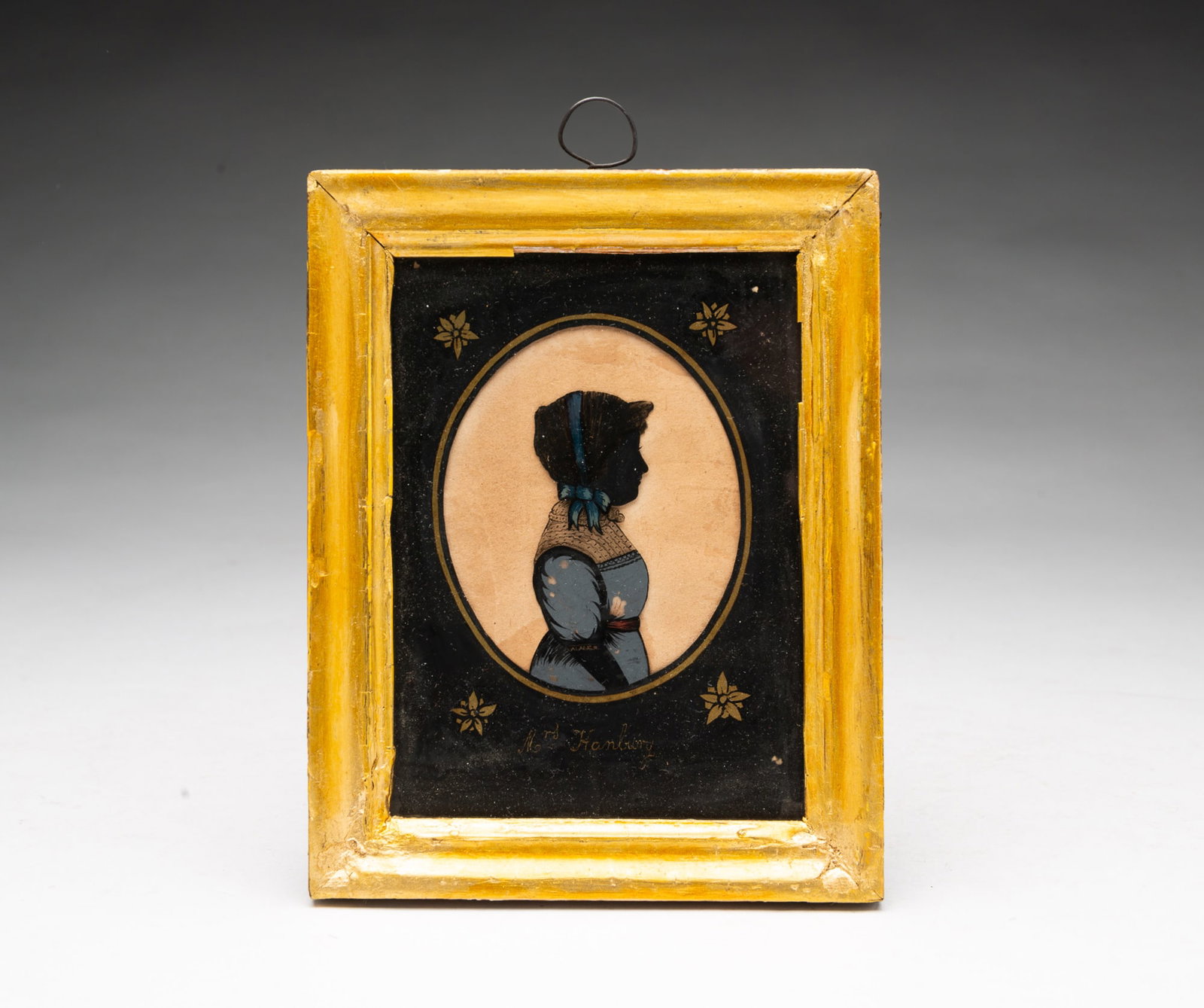 REVERSE-PAINTED GLASS SILHOUETTE OF "MRS. HANBURY" WITH EGLOMISE FRAME.: REVERSE-PAINTED GLASS SILHOUETTE OF "MRS. HANBURY" WITH EGLOMISE FRAME. American, 19th Century. Reverse glass-painted silhouette. Blue dress, fine detail of bodice, wearing a bonnet with a blue