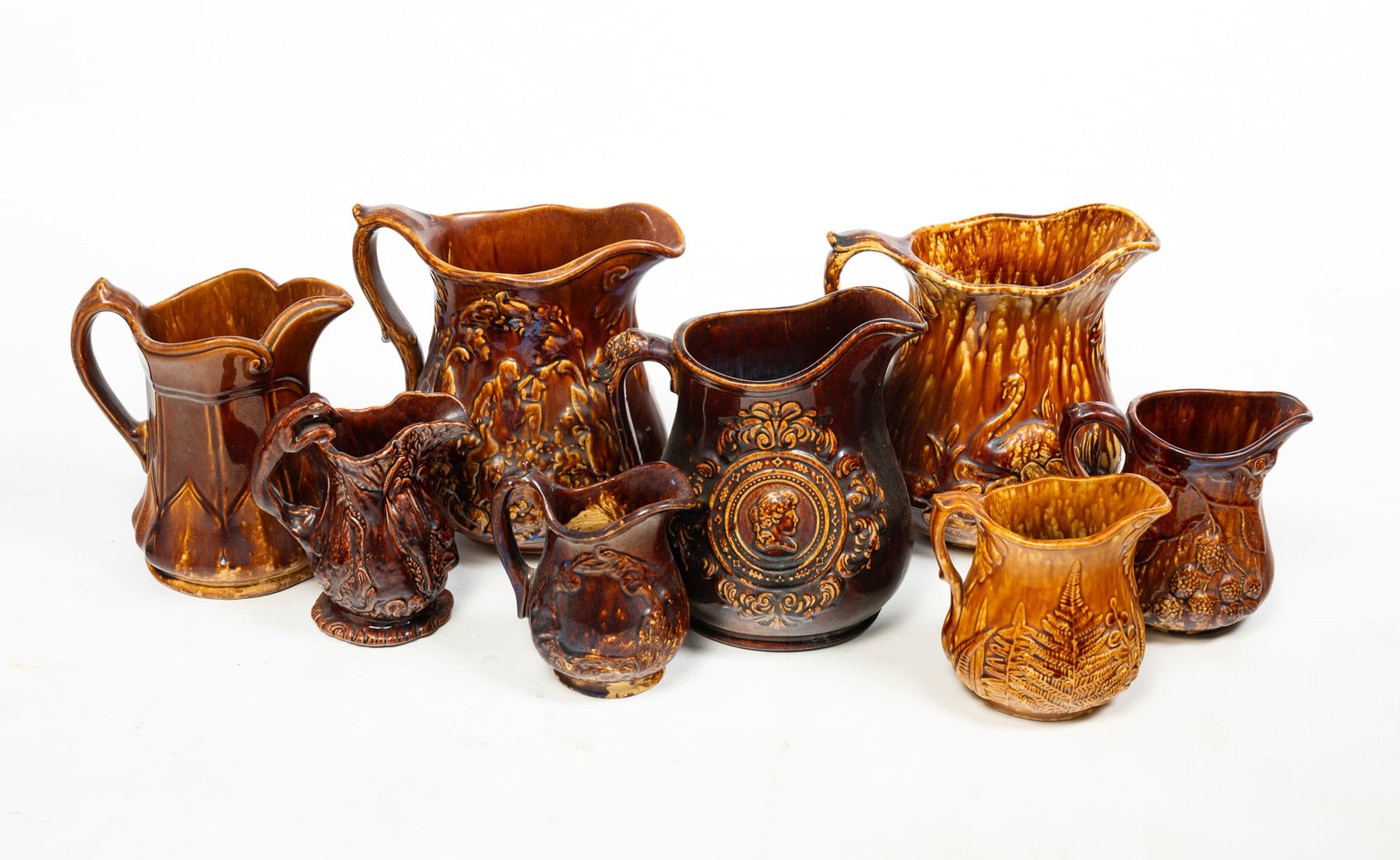 EIGHT ROCKINGHAM PITCHERS AND CREAMERS.: EIGHT ROCKINGHAM PITCHERS AND CREAMERS. American, 19th Century. Yellowware with mottled brown glaze. Features hunt scenes, portraits, animals, and geometric patterns. From 10"h. to 5.5"h. Provenance: