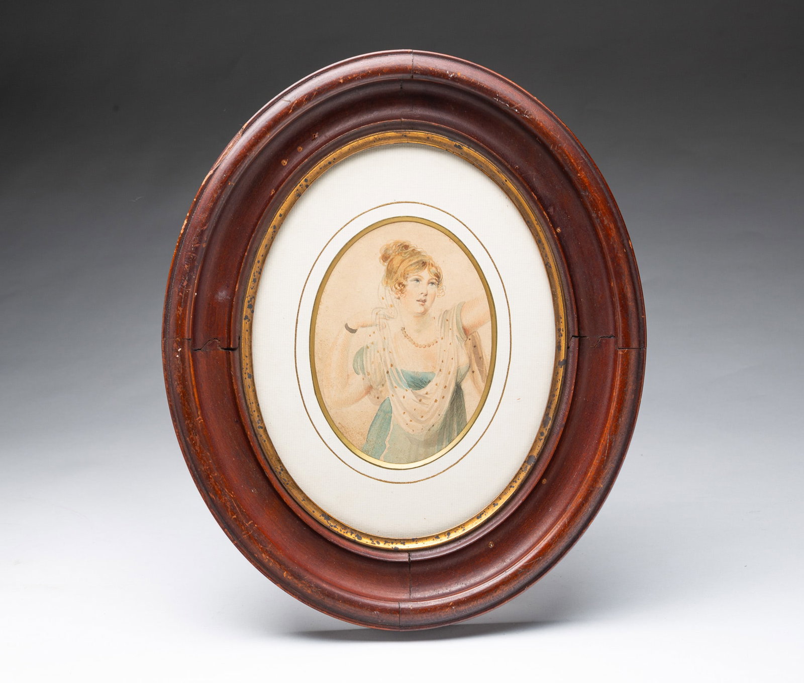 WATERCOLOR PORTRAIT OF A YOUNG LADY IN AN OVAL FRAME.: WATERCOLOR PORTRAIT OF A YOUNG LADY IN AN OVAL FRAME. English, 19th Century. She has blue eyes and her blond hair up with cascading ringlets, wearing a sheer polka-dotted scarf, beaded necklace, and