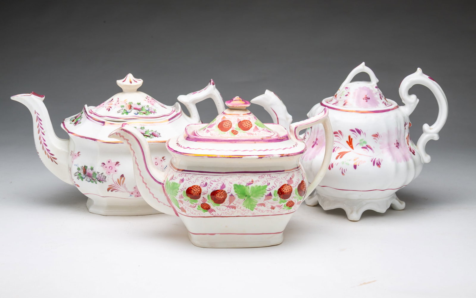 THREE PINK LUSTERWARE TEAPOTS.: THREE PINK LUSTERWARE TEAPOTS. England, 19th Century. Two with squared bodies; floral decoration on one and strawberries on the other, and the third, round in form and decorated with flowers, 7.5"h.