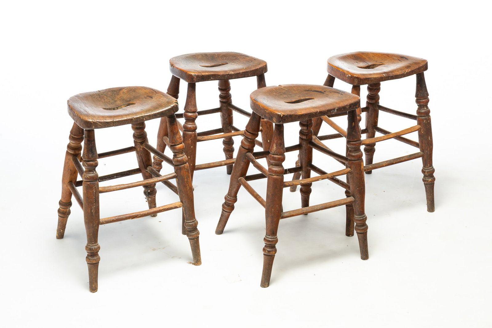FOUR "SADDLE-SEAT" TAVERN STOOLS WITH TURNED LEGS.: FOUR "SADDLE-SEAT" TAVERN STOOLS WITH TURNED LEGS. English, 19th Century. Elm. Shaped seats with hand grips and boldly turned legs. 20.5"h. Provenance: The Lifetime Collection of Martha Magsig Lynch
