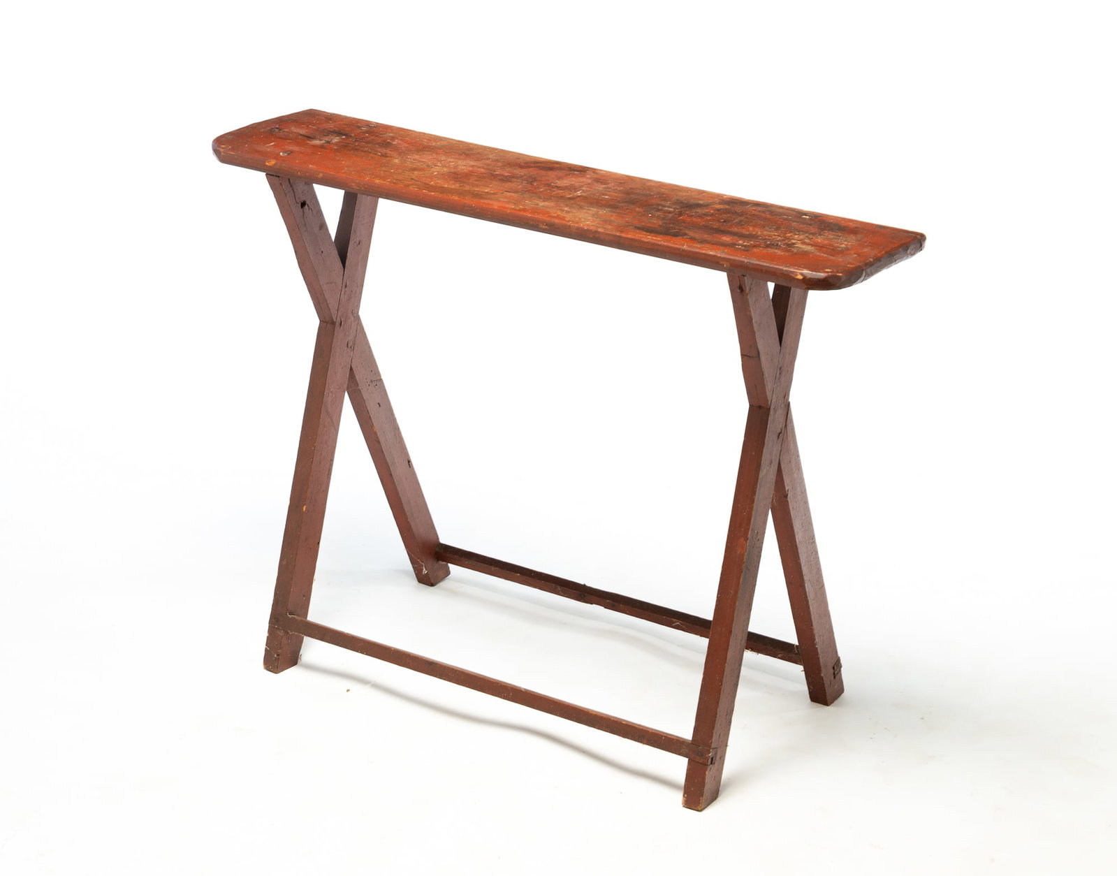 STAND WITH SAWBUCK BASE AND ORIGINAL RUST RED PAINT.: STAND WITH SAWBUCK BASE AND ORIGINAL RUST RED PAINT. American, 19th Century. Pine. Top with rounded corners, "X" ends, and square stretchers. 26"h. 34.25"w. 8"d. Provenance: The Lifetime Collection