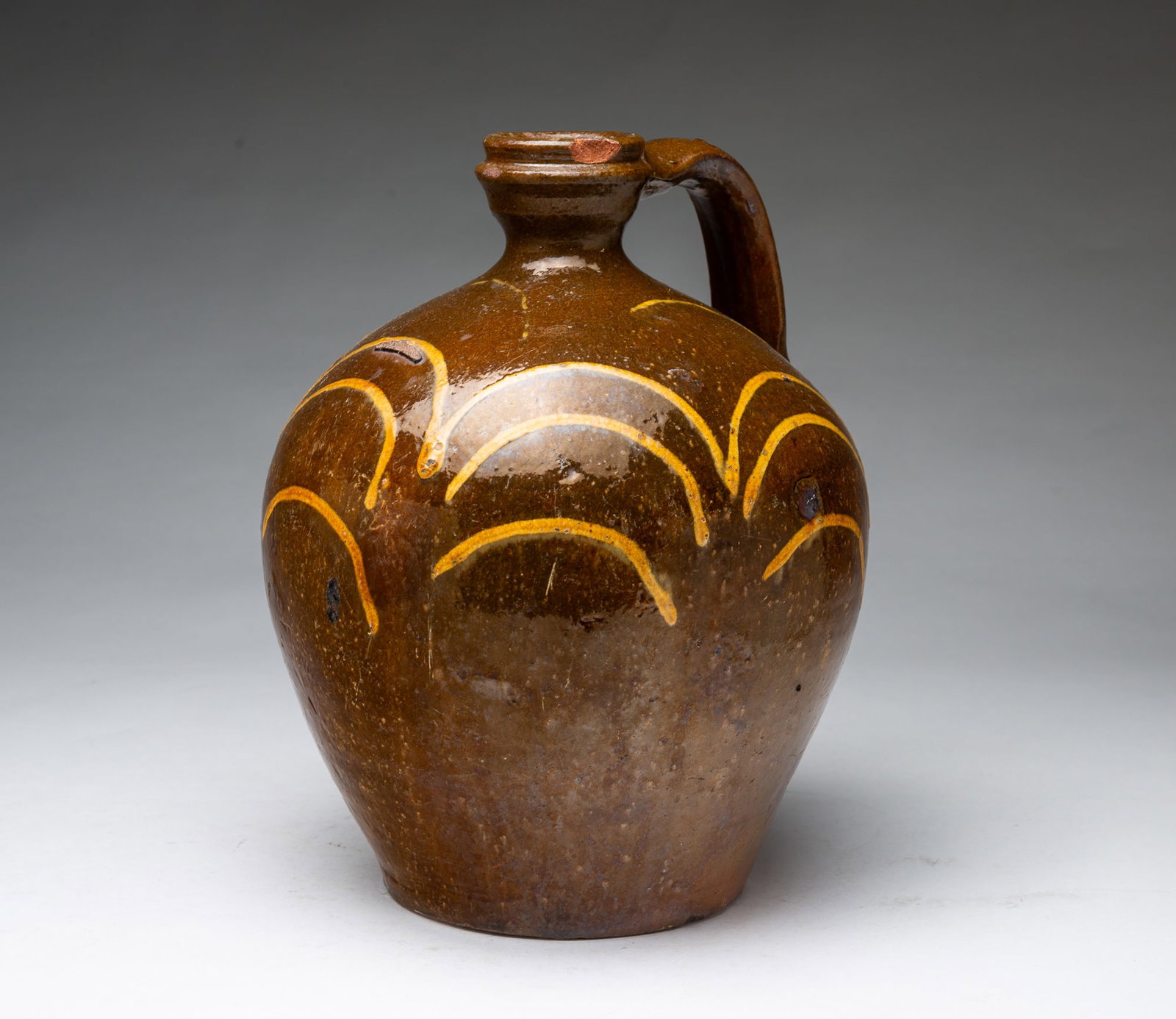 REDWARE JUG WITH SLIP DECORATION.: REDWARE JUG WITH SLIP DECORATION. American,19th Century. Of bulbous form with applied strap handle, and slip-traced decoration. 10"h.
