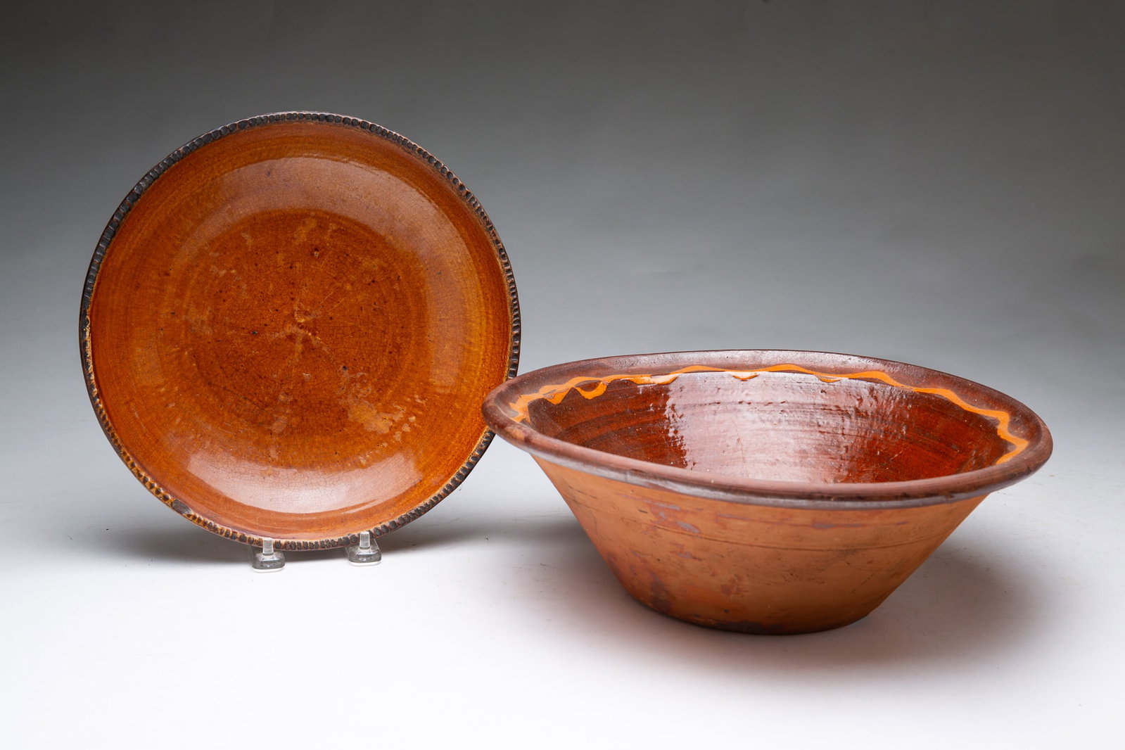 TWO REDWARE BOWLS.: TWO REDWARE BOWLS. American, 19th Century. Mixing bowl with glazed interior and squiggly slip line around rim, 5"h. 12.25"d., and a pie plate with coggled rim, reddish-brown interior, and tan