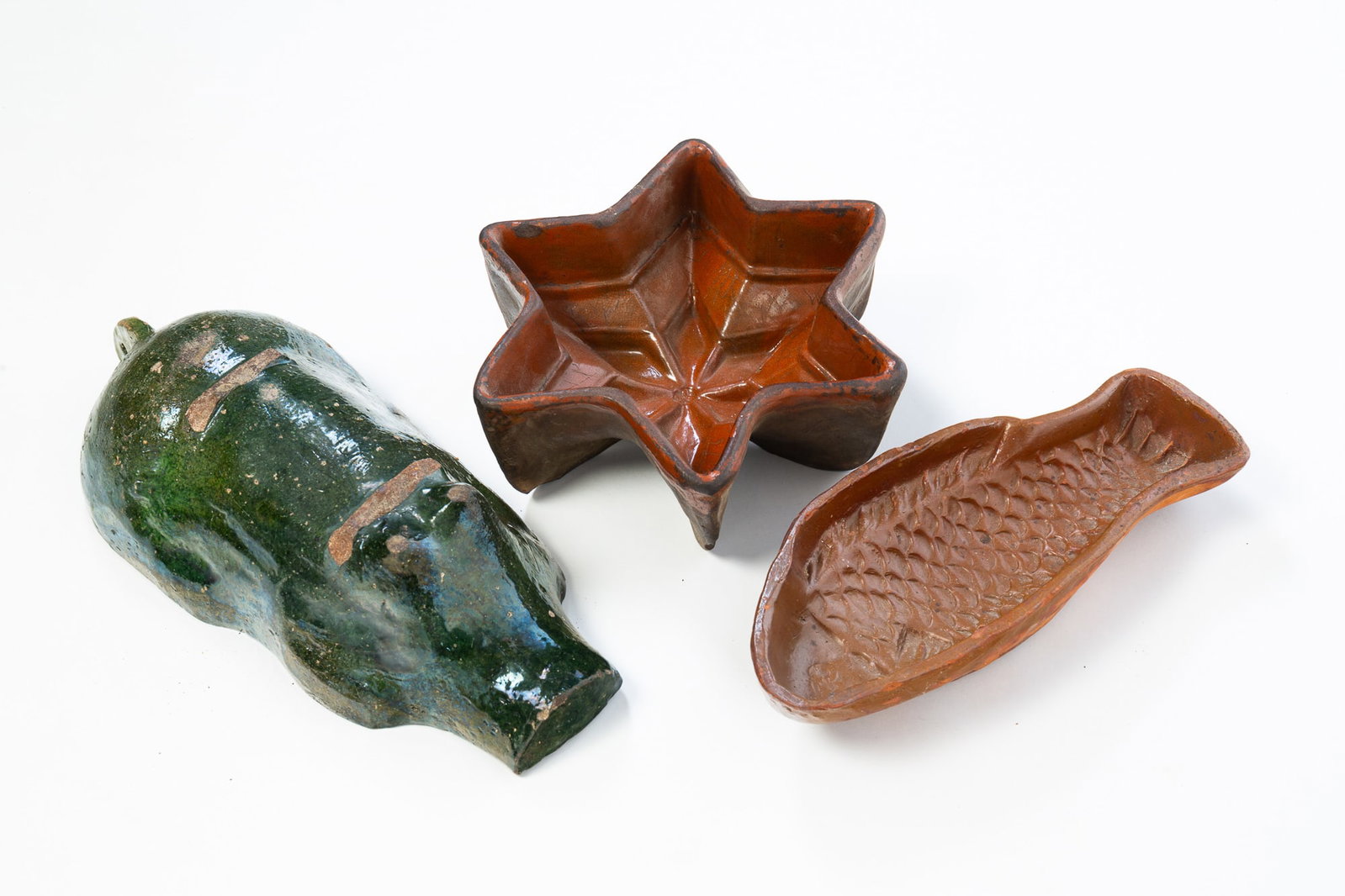 THREE EUROPEAN REDWARE FOOD MOLDS.: THREE EUROPEAN REDWARE FOOD MOLDS. 19th Century. A fish with brown glaze, 2.5"h. 12"w., a star with orange glaze, 3.5"h. 10" across, and pig mold with green glaze, 3"h. 14.5"w. Provenance: The