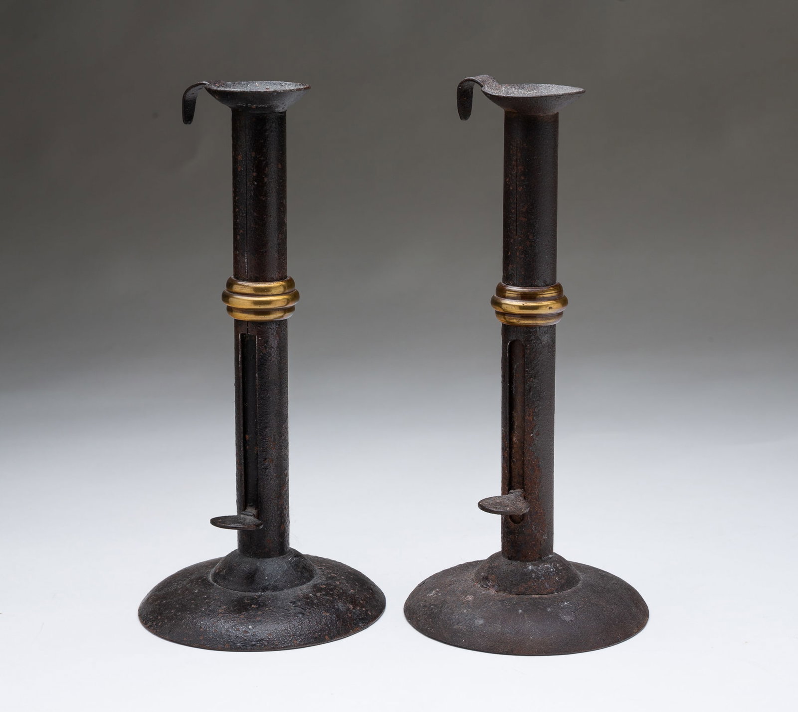 PAIR OF REPRODUCTION HOGSCRAPER WEDDING BAND PUSHUP CANDLESTICKS.: PAIR OF REPRODUCTION HOGSCRAPER WEDDING BAND PUSHUP CANDLESTICKS. American or English, 20th Century. Circular bases, shafts with push-ups, candle sockets, and thumb grips. 9"h.