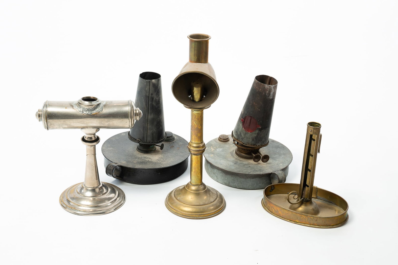 FOUR METAL FLUID LAMPS AND A CHAMBERSTICK.: FOUR METAL FLUID LAMPS AND A CHAMBERSTICK. American, 19th Century. Includes brass, tin, and a silvered metal example. Tallest, 14.5"h. Provenance: The Lifetime Collection of Richard & Phyllis Zirbel