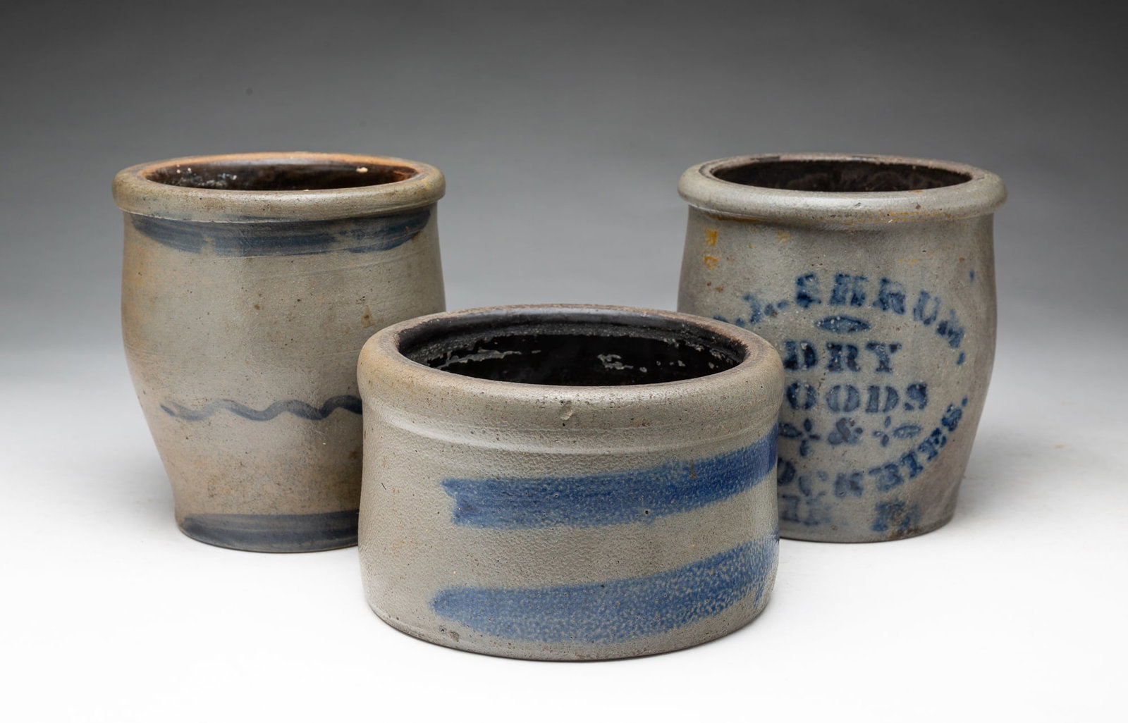 THREE COBALT-DECORATED STONEWARE JARS.: THREE COBALT-DECORATED STONEWARE JARS. American, Second half 19th Century. A butter crock with rolled lip and two cobalt freehand stripes, 4.25"h. 7"w., a jar with ovoid form, rolled lip, and cobalt f