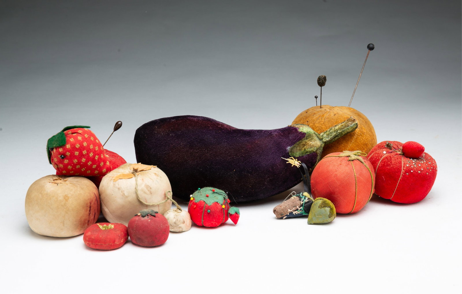 COLLECTION OF FRUIT AND VEGETABLE SHAPED PINCUSHIONS.: COLLECTION OF FRUIT AND VEGETABLE SHAPED PINCUSHIONS. American, 19th and 20th Centuries. Eggplant with grasshopper stickpin, orange, five tomatoes, three strawberries, and two turnips. From 9"h. to