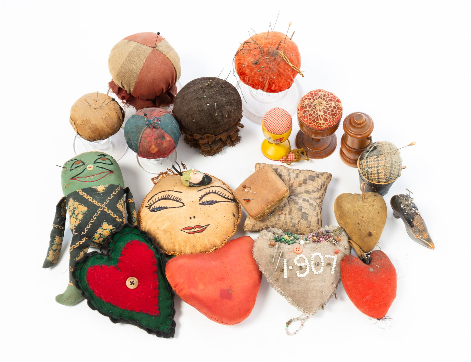 COLLECTION OF PINCUSHIONS AND SEWING ACCOUTREMENTS.: COLLECTION OF PINCUSHIONS AND SEWING ACCOUTREMENTS. American, 19th and 20th Centuries. Five are make-dos on glass bases, five are heart-shaped with bead work dated 1907, doll shape, two in turned gobl