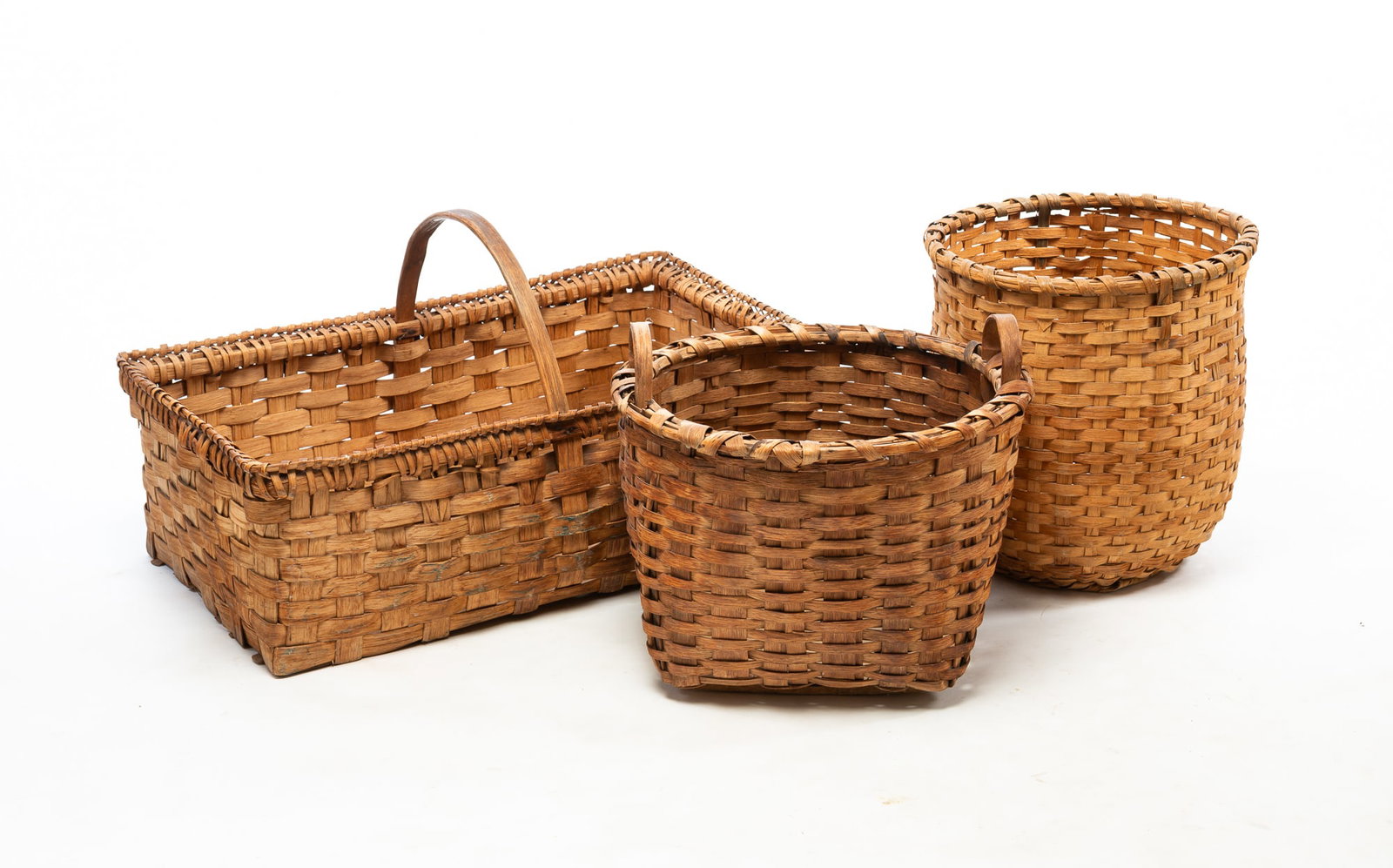 THREE LARGE WOVEN SPLINT BASKETS.: THREE LARGE WOVEN SPLINT BASKETS. American, Late 19th Century. A large rectangular basket with wrapped rim and a bentwood handle, 17"h. 31"w., a gathering basket with two bentwood handles and a