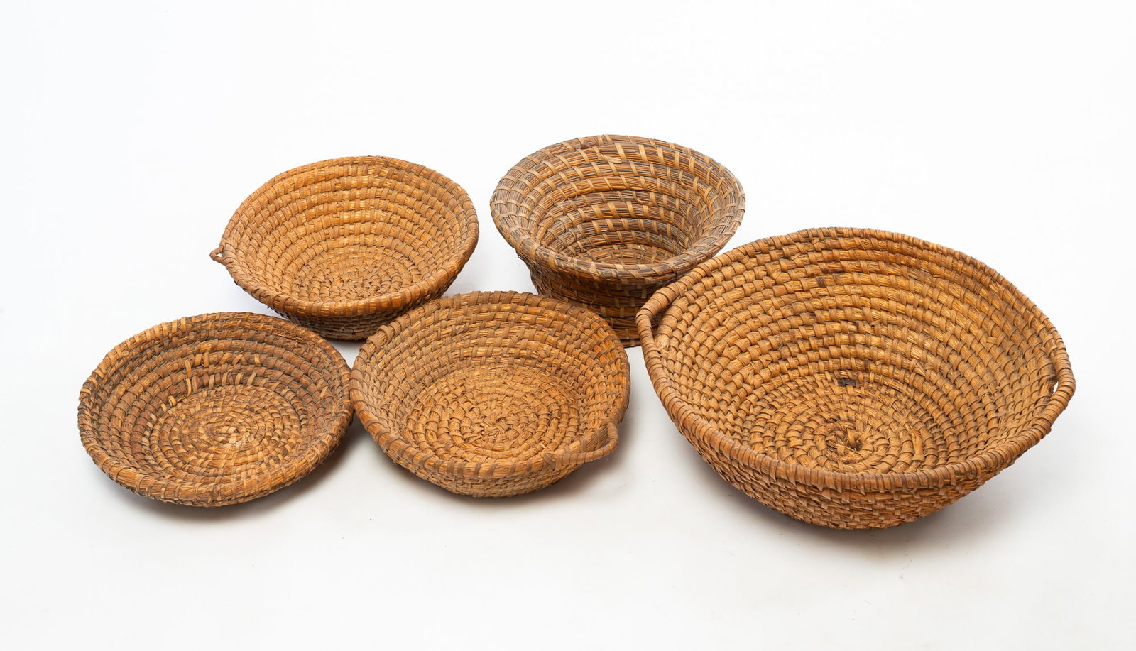 FIVE RYE STRAW BASKETS.: FIVE RYE STRAW BASKETS. American, Late 19th and 20th Centuries. The largest with handles. 7.5"h. 20" across handles, two with single handle, 4.5"h. 13.75" and 4"h. 14.5" across, shallow, 3.5"h.