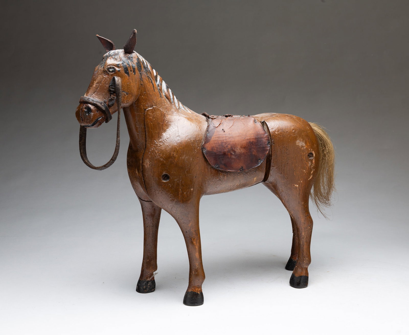 FOLK ART CARVED AND PAINTED WOODEN HORSE.: FOLK ART CARVED AND PAINTED WOODEN HORSE. American, 20th Century. Standing carved wooden horse made of several parts screwed together, with leather ears, reins, and saddle and a horsehair tail, painte