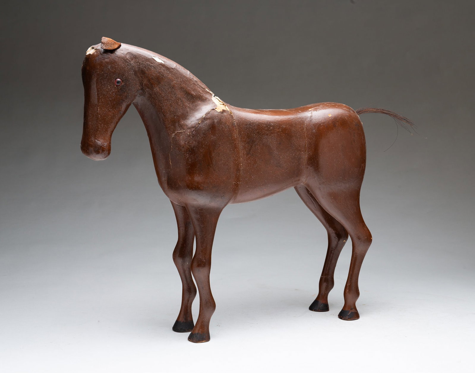 FOLK ART CARVED AND PAINTED WOODEN HORSE.: FOLK ART CARVED AND PAINTED WOODEN HORSE. American, early 20th Century. Standing carved wooden horse covered in brown-painted plaster, with leather ears, a horsehair tail, and black-painted hooves. 15