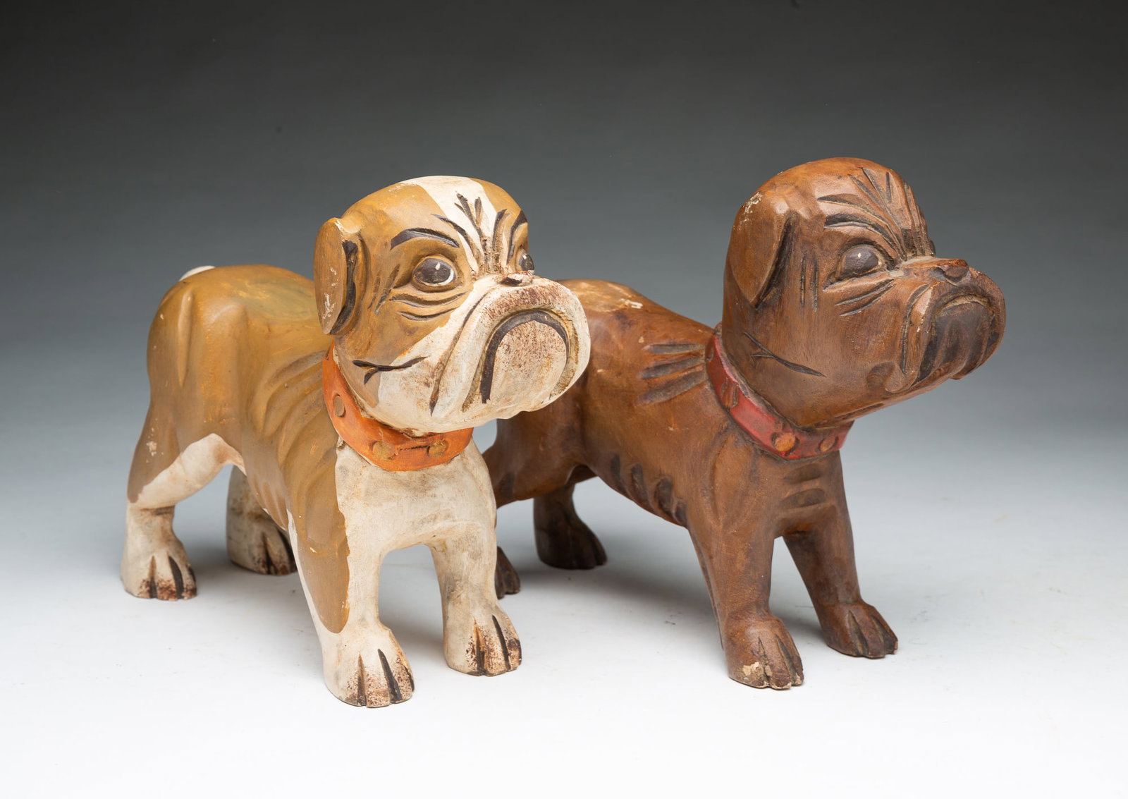 PAIR OF FOLK ART CARVED AND PAINTED WOODEN BULL DOGS.: PAIR OF FOLK ART CARVED AND PAINTED WOODEN BULL DOGS. American, 19th or 20th Century. Each carved in standing position on all fours with furrowed brows and downturned mouths. One painted tan and
