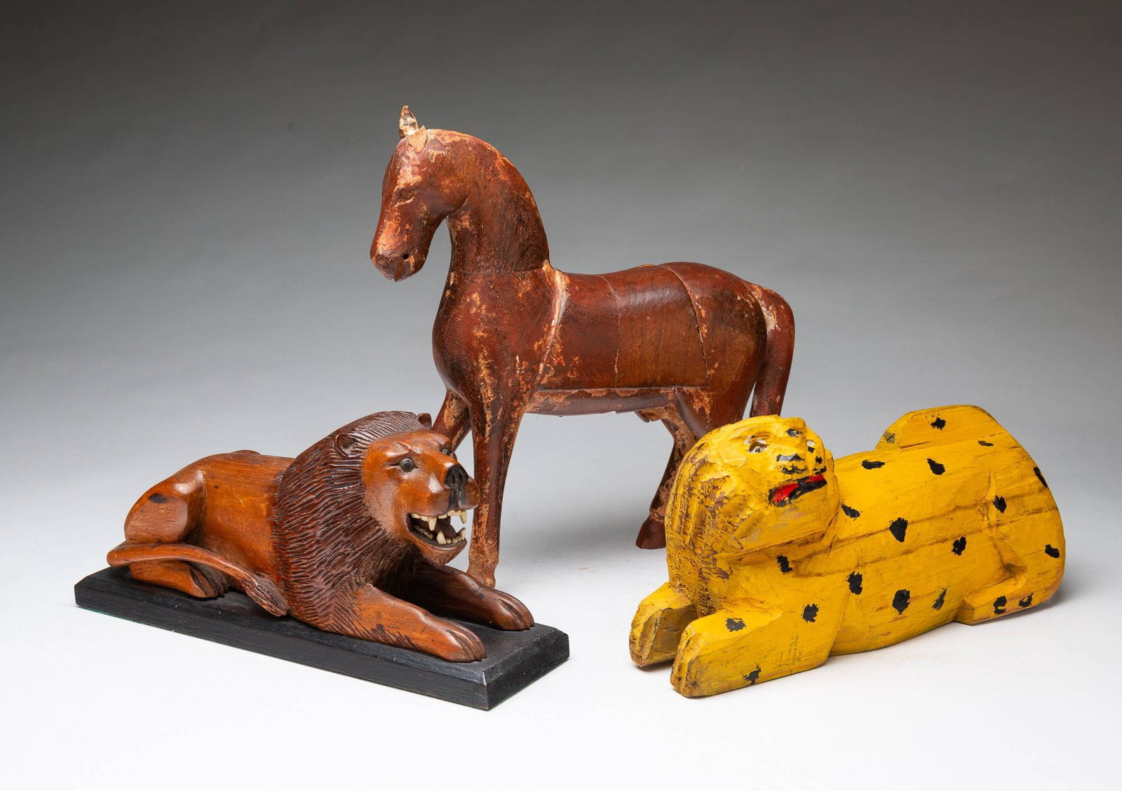 GROUP OF CARVED WOOD ANIMAL FIGURES WITH A HORSE AND TWO LIONS.: GROUP OF CARVED WOOD ANIMAL FIGURES WITH A HORSE AND TWO LIONS. American, 20th Century. A horse figure, 11"h. A lion carved in a naturalistic pose with a detailed mane, mounted on a black base, and a
