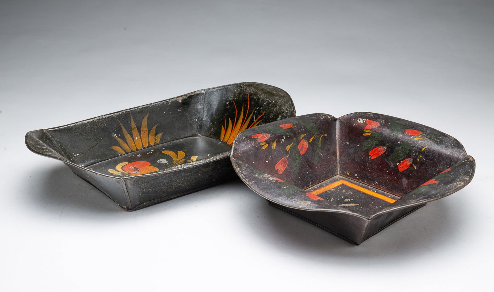 TWO TOLE APPLE TRAYS.: TWO TOLE APPLE TRAYS. American, 19th Century. One in square form with rolled rounded sides, and decorated with flowers and yellow striping, 2.25"h. 10.25"w., together with an oblong tray with rolled