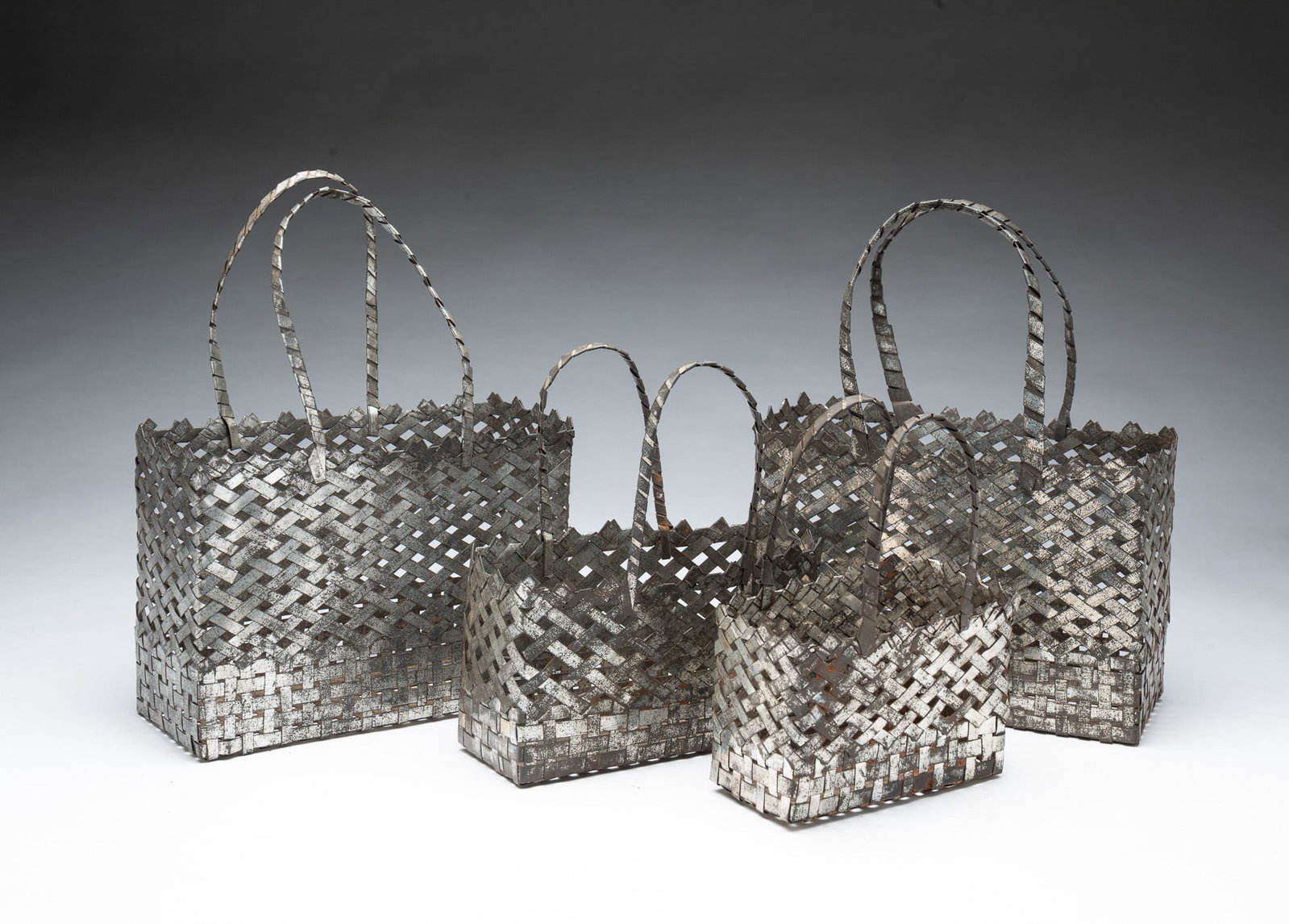 SET OF FOUR HAND-WOVEN TIN ANNIVERSARY BASKETS WITH HANDLES.: SET OF FOUR HAND-WOVEN TIN ANNIVERSARY BASKETS WITH HANDLES. American, Early 20th Century. Each of rectangular form with woven sides and bottom, the handles twisted and flattened. In four sizes. Two