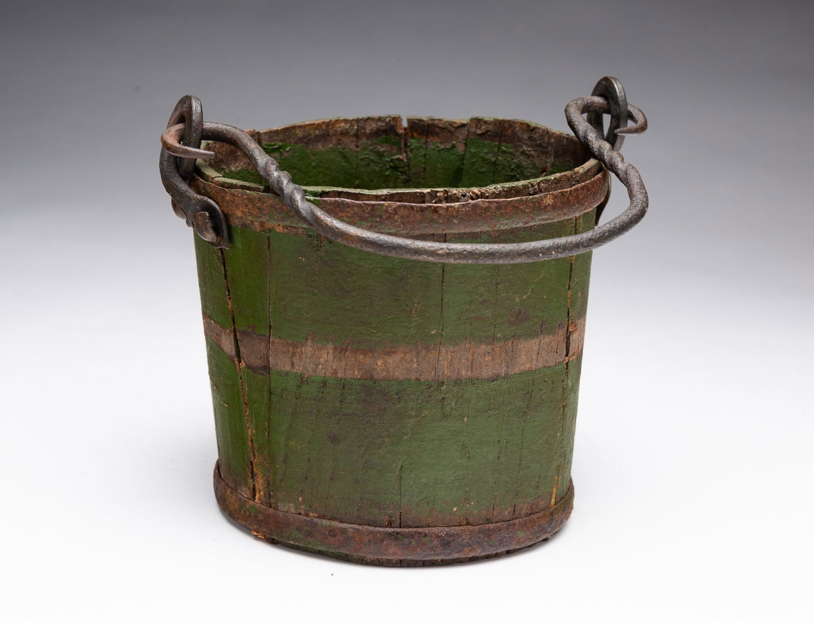 DIMINUTIVE BERRY BUCKET WITH FORGED IRON HANDLE IN OLD GREEN PAINT.: DIMINUTIVE BERRY BUCKET WITH FORGED IRON HANDLE IN OLD GREEN PAINT. American, 19th Century. Stave-constructed with iron hoops and a twisted forged iron handle that hooks into overlapping iron loops