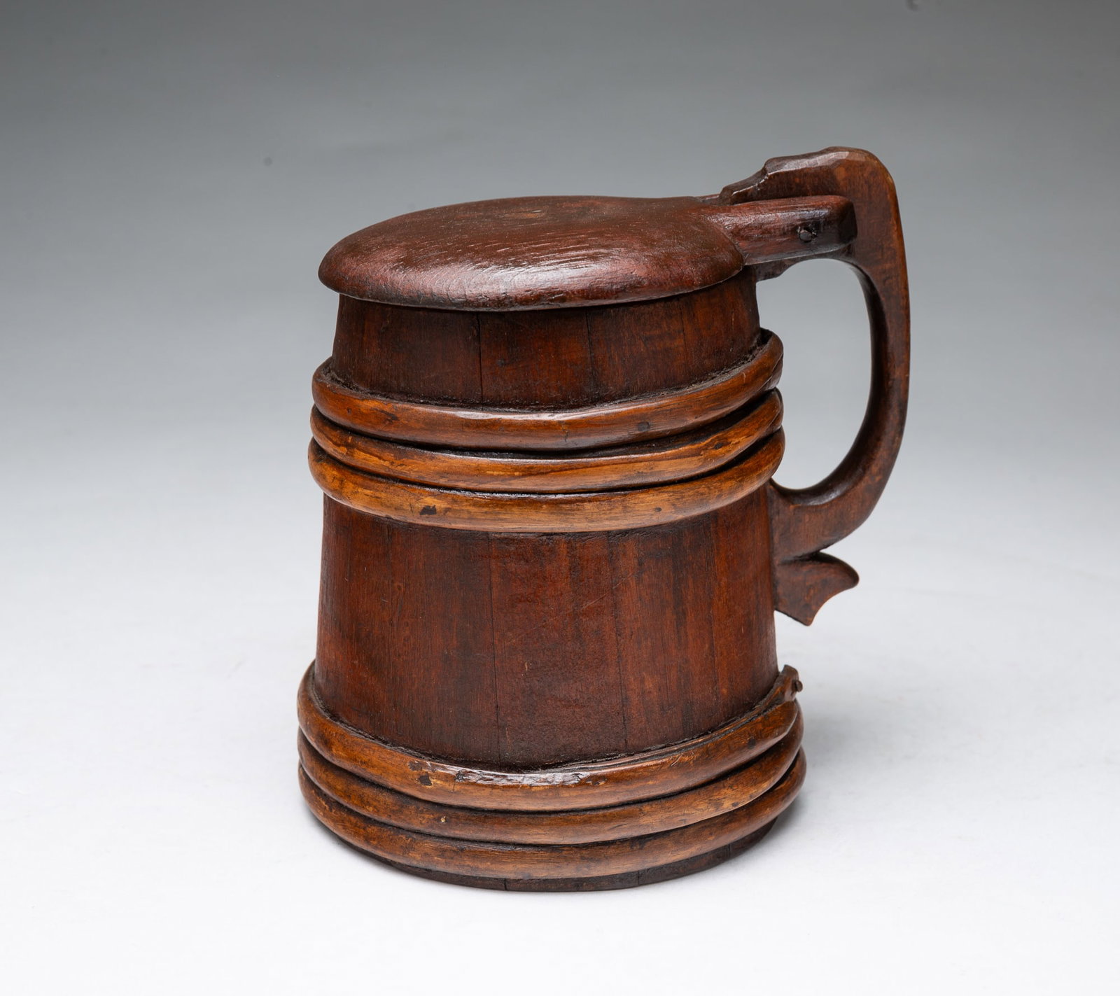 STAVE CONSTRUCTED LIDDED TANKARD.: STAVE CONSTRUCTED LIDDED TANKARD. American, Late 19th Century. Stave constructed lidded tankard crafted from wood. The piece features a hinged lid and single handle, with multiple raised bands