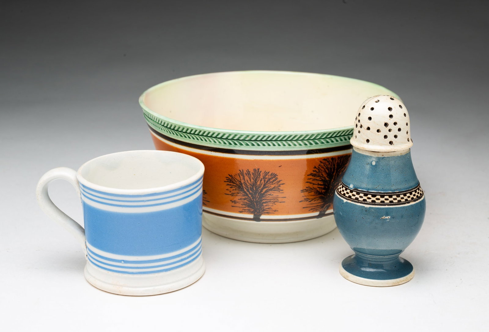 THREE MOCHAWARE ITEMS.: THREE MOCHAWARE ITEMS. American, Late 19th or Early 20th Centuries. A large bowl with impressed border, seaweed decoration, and a flared foot, 4.25"h. A muffineer with a blue ground and a band with