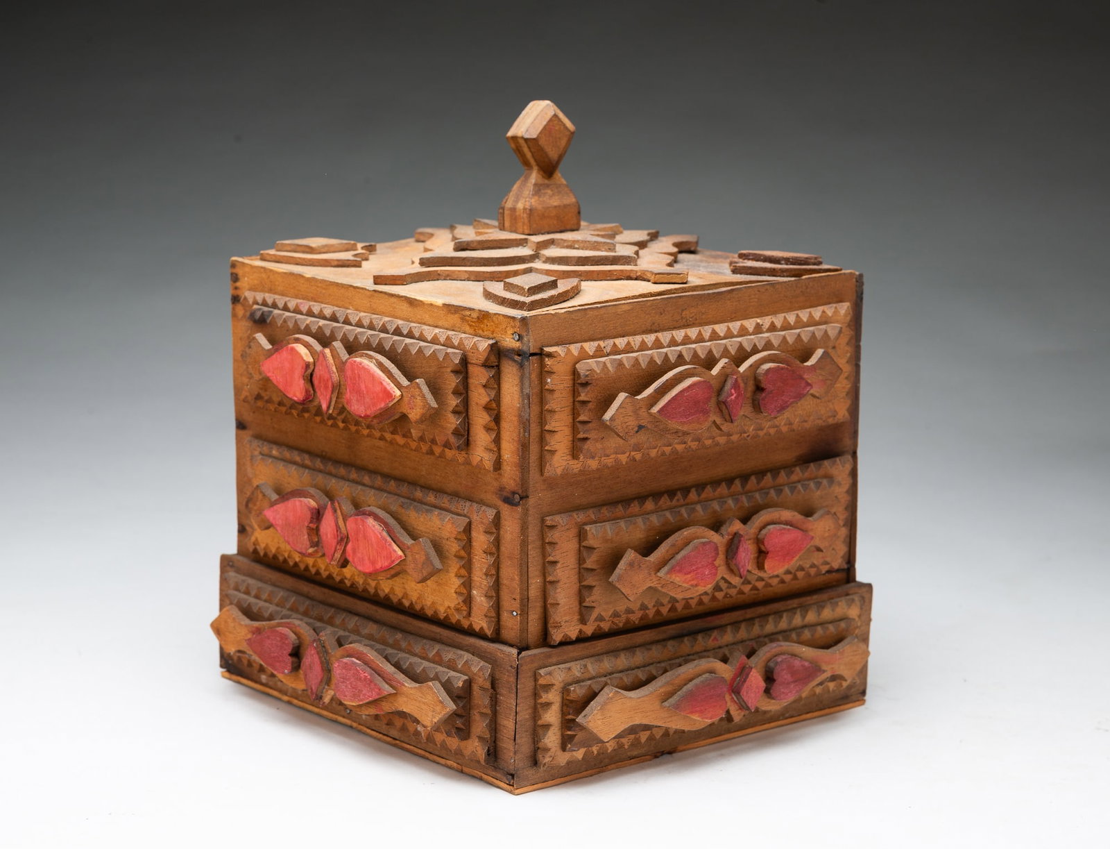 FOLKSY TRAMP ART PAINTED AND CHIP-CARVED LIDDED BOX WITH HEARTS AND DIAMONDS.: FOLKSY TRAMP ART PAINTED AND CHIP-CARVED LIDDED BOX WITH HEARTS AND DIAMONDS. American, 20th Century. Pine. The lift-off lid having a laminated and diamond-shaped finial with layered shapes in center 