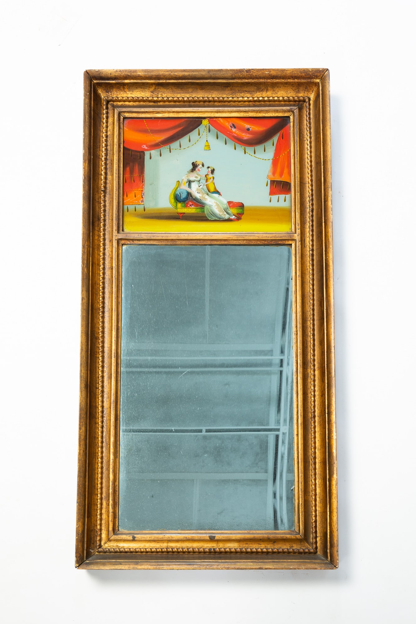 EMPIRE MIRROR WITH REVERSE PAINTED TABLET.: EMPIRE MIRROR WITH REVERSE PAINTED TABLET. American, 19th Century. Gilded coved frame with rope twist detail, tablet with a lady reclining on a chaise lounge holding her daughter on a red draped