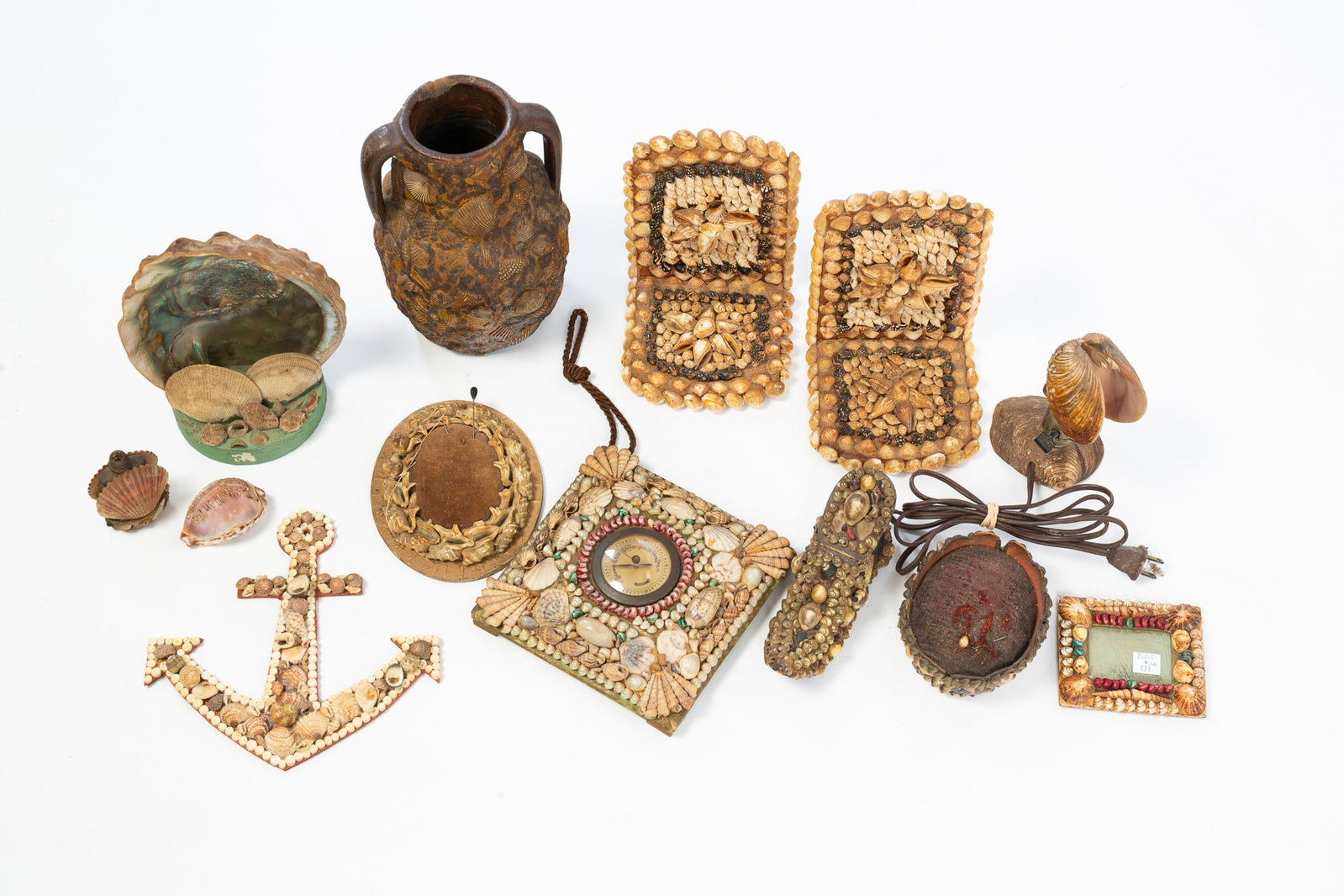 TWELVE SHELL ART ITEMS.: TWELVE SHELL ART ITEMS. 20th Century. Stoneware open handle jar encrusted with shells, 8.75"h., pair of bookends, 6.5"h., a lamp, 6"h., anchor-shaped wall hanging, 8.25"h., abalone shell candle