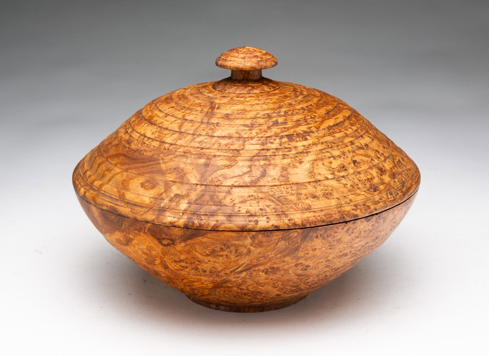 TURNED BURL COVERED BOWL.: TURNED BURL COVERED BOWL. American, 20th Century. Footed bowl with incised banding, lid with banding, and knob finial. Impressed markers mark to bottom. 6"h. 8"d. Provenance: From the Lifetime