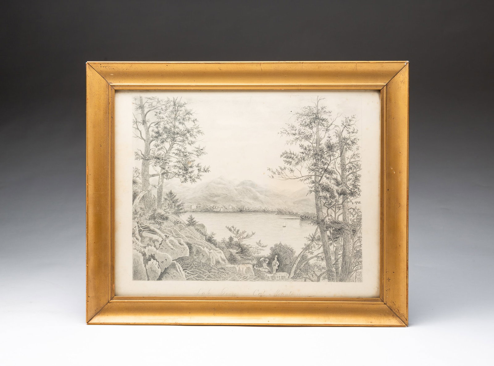 PENCIL ON PAPER DRAWING OF LAKE GEORGE.: PENCIL ON PAPER DRAWING OF LAKE GEORGE. American, 19th Century. Depicting a serene lake view with two figures on a rocky bank surrounded by trees and bushes, with the lake beyond them and mountains