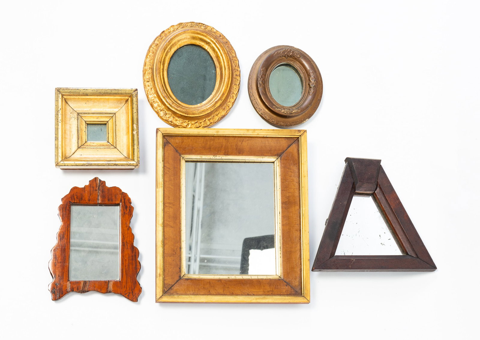 SIX DIMINUTIVE MIRRORS.: SIX DIMINUTIVE MIRRORS. American, 19th Century. Two are oval with gold frames, 7"h. 6"w., and 9"h. 7.75"w., gold edge and liner with grain painted beveled section, 13.5"h. 11.5"w., square gold leafed,