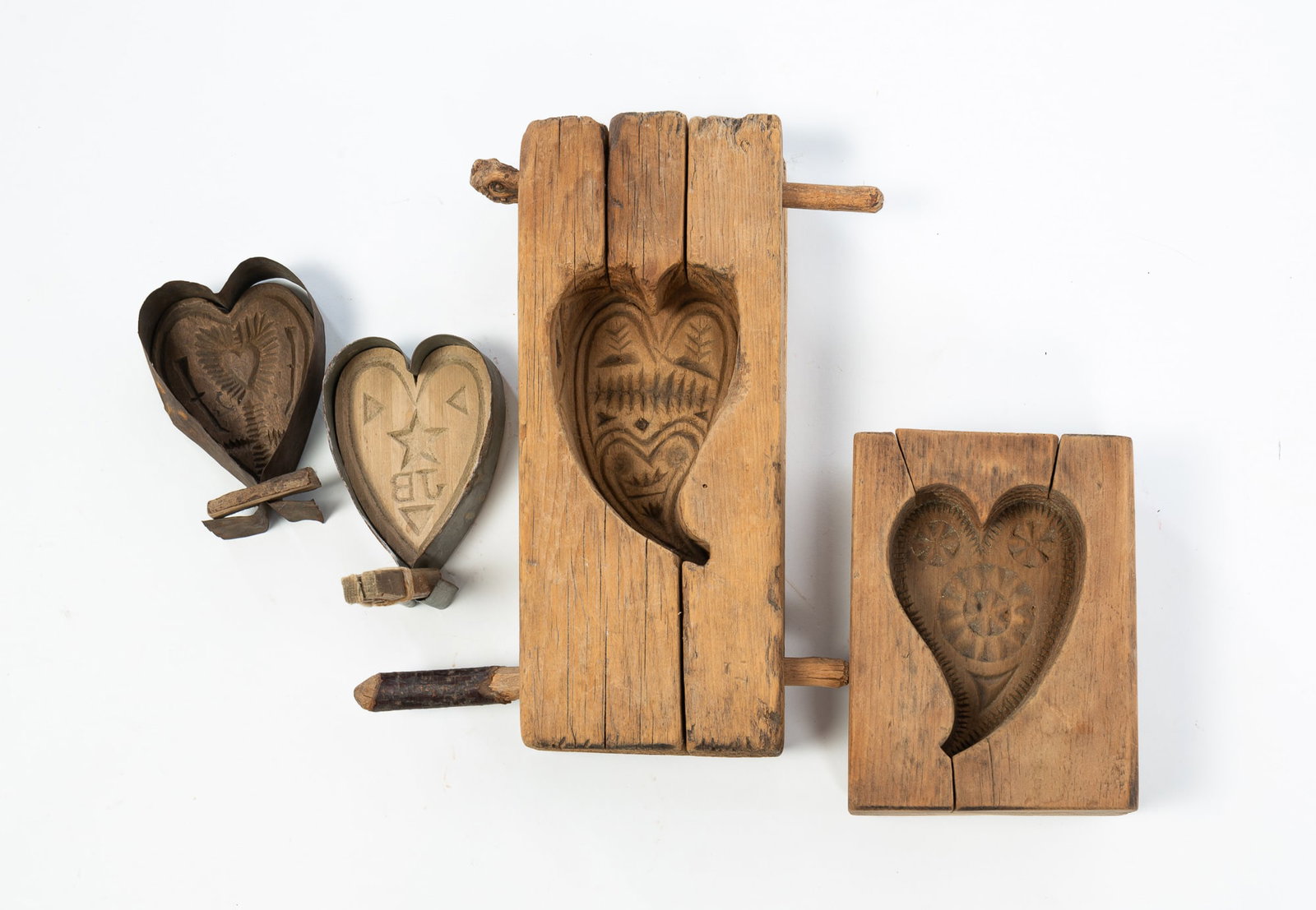 FOUR HEART-FORM MAPLE SUGAR MOLDS.: FOUR HEART-FORM MAPLE SUGAR MOLDS. Two with metal sides, one with a heart and flower motif, the other with the initials "JB" with triangles and stars. Two larger wooden cased molds, one with leaves
