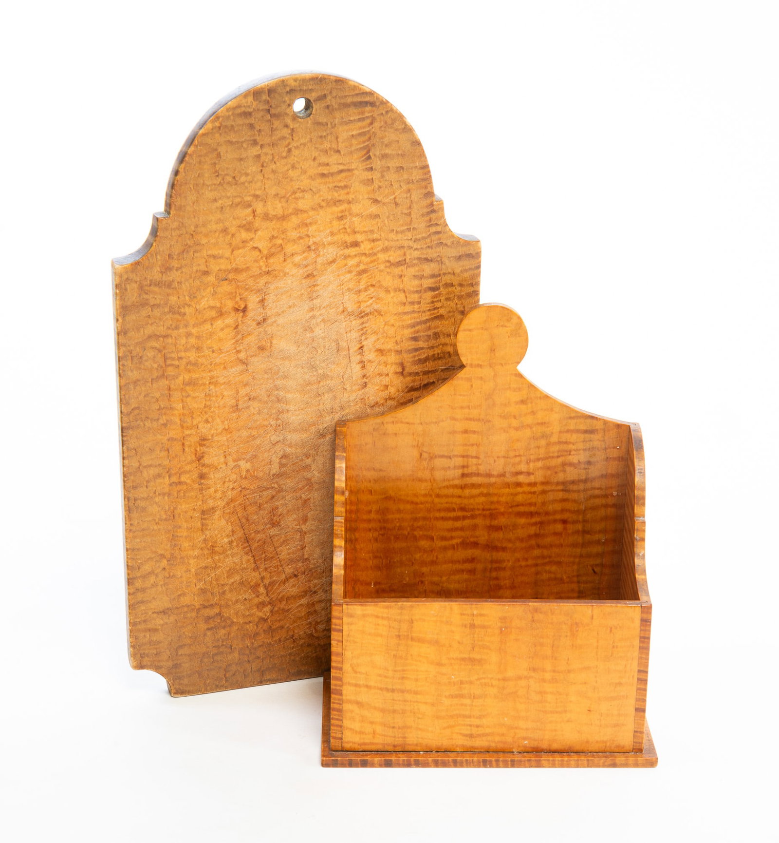 TIGER MAPLE CUTTING BOARD AND CANDLE BOX.: TIGER MAPLE CUTTING BOARD AND CANDLE BOX. American, Late 19th or Early 20th Century. A cartouche-shaped cutting board with a hole at top, 15"h. 8.75"w. Together with a tabletop candle box with a lolli