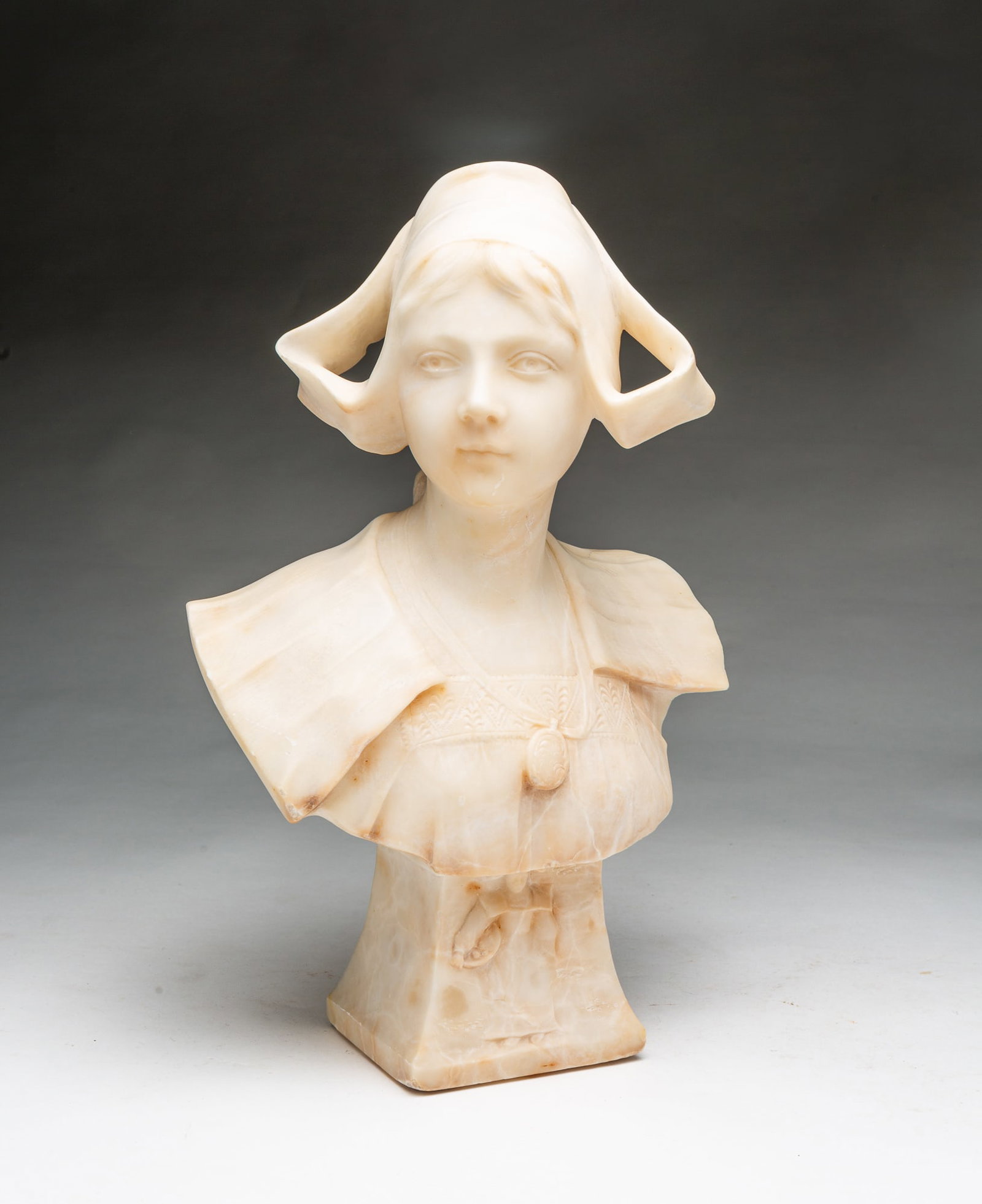VICTORIAN CARVED ALABASTER BUST OF A YOUNG WOMAN.: VICTORIAN CARVED ALABASTER BUST OF A YOUNG WOMAN. European, Late 19th Century. Alabaster bust of a young woman wearing a Dutch-style hat, a locket necklace, and with a large collar on a tapered square