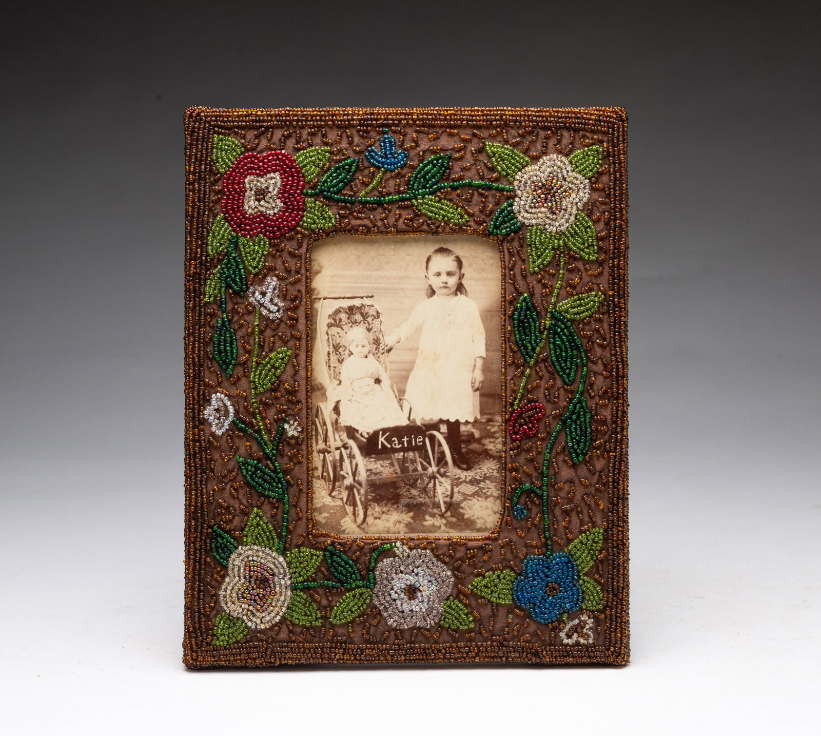 POLYCHROME BEADED PICTURE FRAME WITH FLOWERS AND EARLY PHOTOGRAPH OF A YOUNG GIRL WITH HER DOLL. (1 of 4)