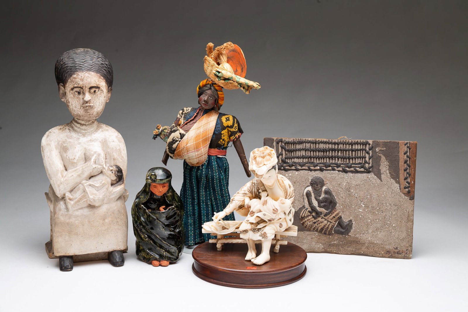 FIVE FIGURINES OF NURSING MOTHERS.: FIVE FIGURINES OF NURSING MOTHERS. 20th Century. An early 20th-century Japanese carved natural material Okimono of seated mother on a wooden stand, signed on base. A carved and painted wood seated