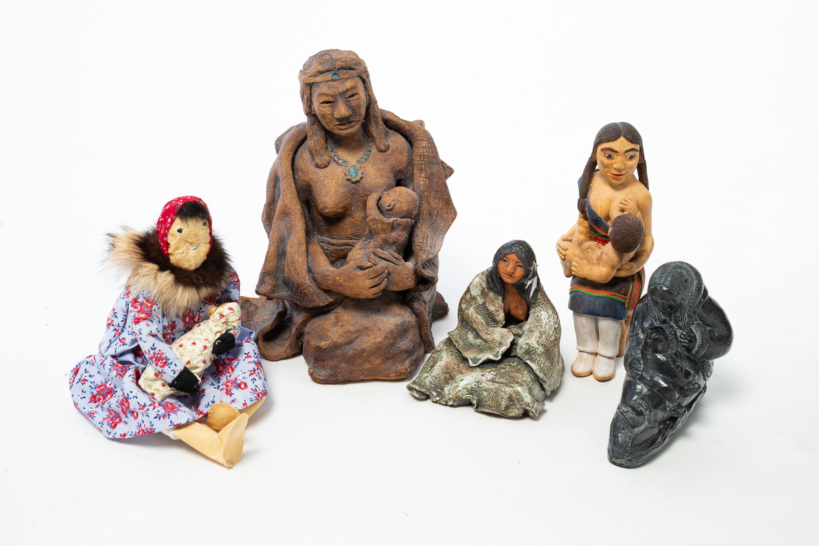 FIVE NATIVE AMERICAN FIGURINES OF NURSING MOTHERS.: FIVE NATIVE AMERICAN FIGURINES OF NURSING MOTHERS. 20th Century. A Canadian stone sculpture by Wolf, a painted wood figure, a leather and cloth figure, and two ceramic figures. Largest, 11"h.