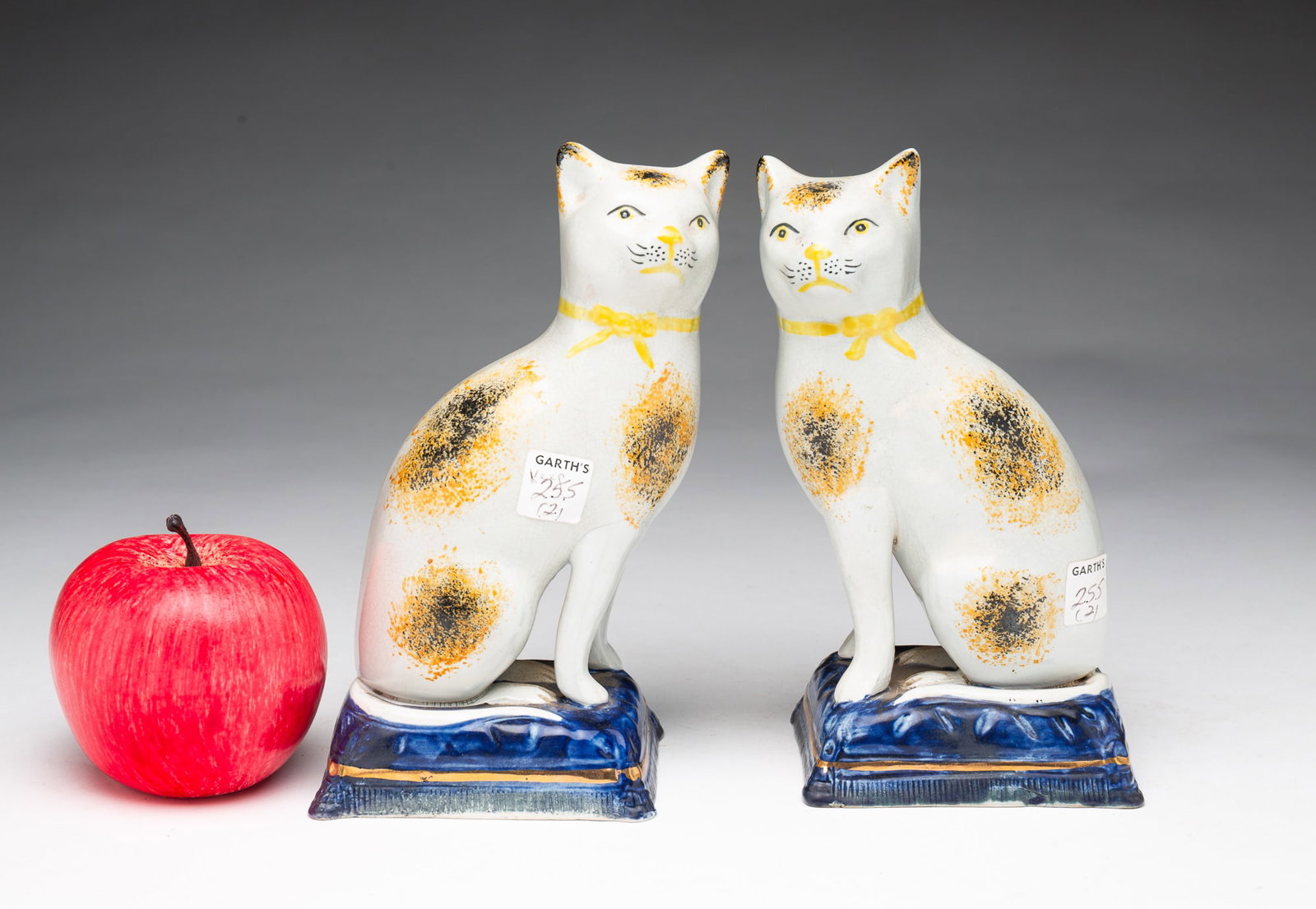 PAIR OF STAFFORDSHIRE POTTERY CATS.: PAIR OF STAFFORDSHIRE POTTERY CATS. English, 19th or 20th Century. With freestanding front legs and seated on blue pillows with gilt trim. Having yellow neck ribbons as well as black and yellow