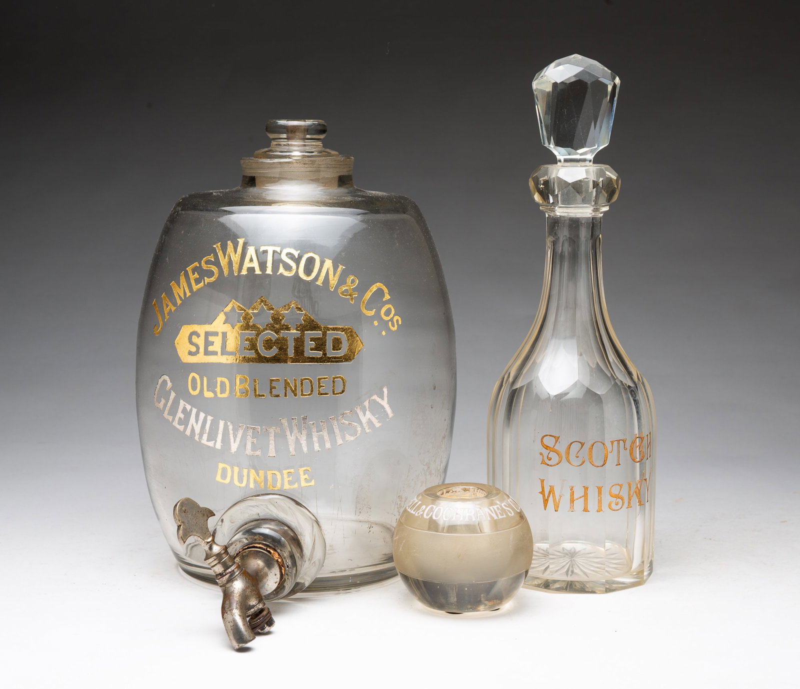 THREE GLASS BAR ACCESSORIES.: THREE GLASS BAR ACCESSORIES. American, 20th Century. A faceted decanter engraved "SCOTCH WHISKY" with faceted stopper, 13"h., a James Watson & Co. Glenlivet Whiskey dispenser with engraved and gilt le