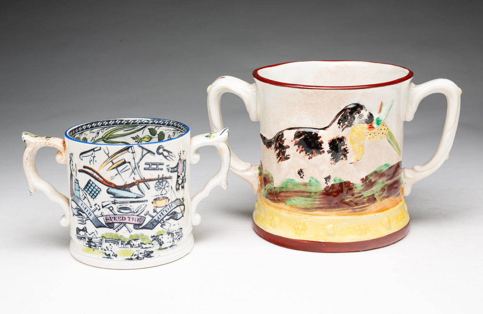 TWO STAFFORDSHIRE DOUBLE HANDLED MUGS.: TWO STAFFORDSHIRE DOUBLE HANDLED MUGS. English, 19th Century. One decorated with farmer's tool and poetic verse and the other with a relief hunt scene with a dog and bird, and a ceramic frog inside,