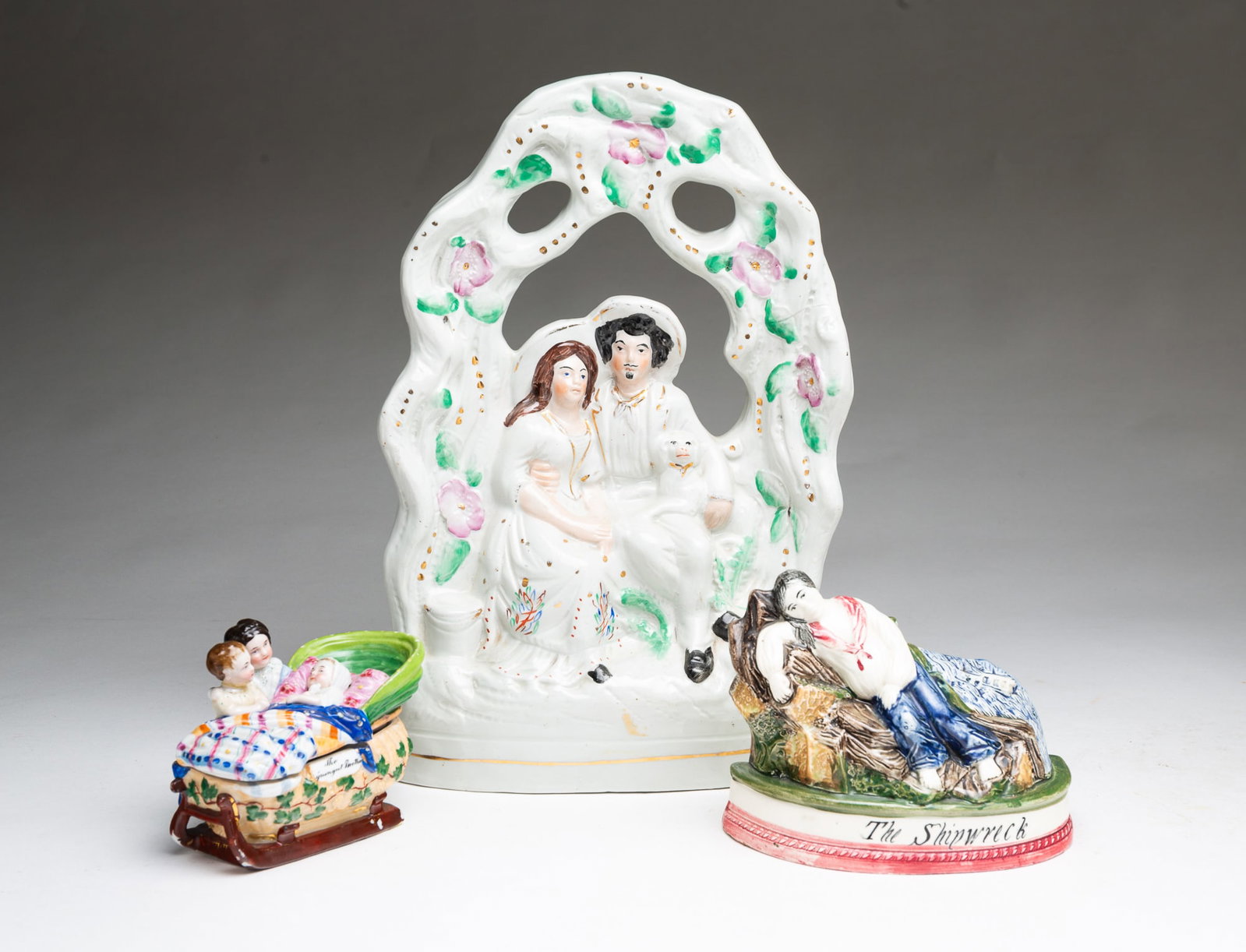 GROUP OF THREE PORCELAIN FIGURINES, INCLUDING STAFFORDSHIRE.: GROUP OF THREE PORCELAIN FIGURINES, INCLUDING STAFFORDSHIRE. England, 19th Century. Staffordshire Courting or Wedding Couple dressed in white with a little dog under a pierced floral arch, polychrome