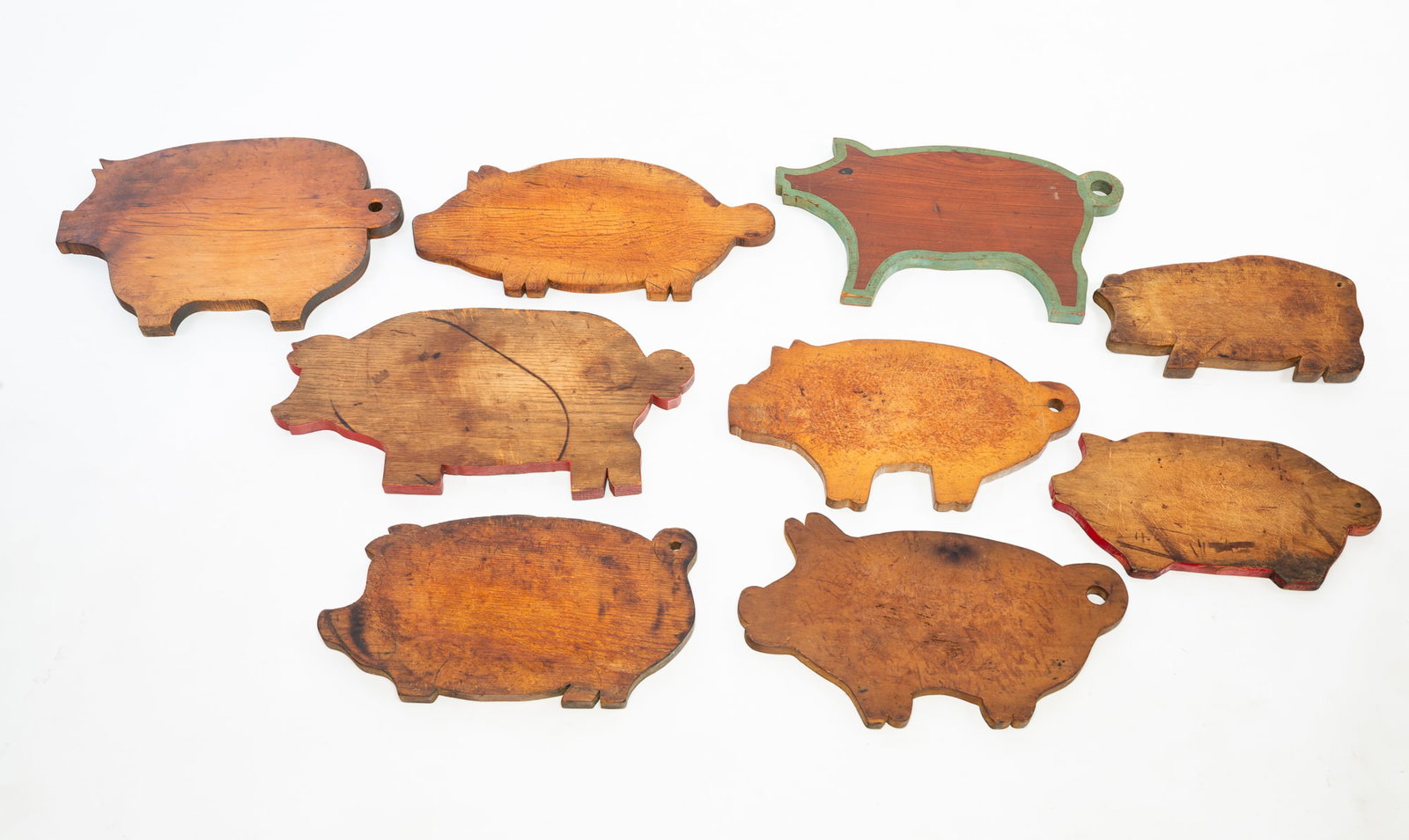 NINE PIG SHAPED CUTTING BOARDS.: NINE PIG SHAPED CUTTING BOARDS. American, 20th Century. Mixed woods. Various sizes, two with painted edges, one with red trim, and seven with ring tails for hanging. From, 19.5"w. to 12.75"w. Provenan