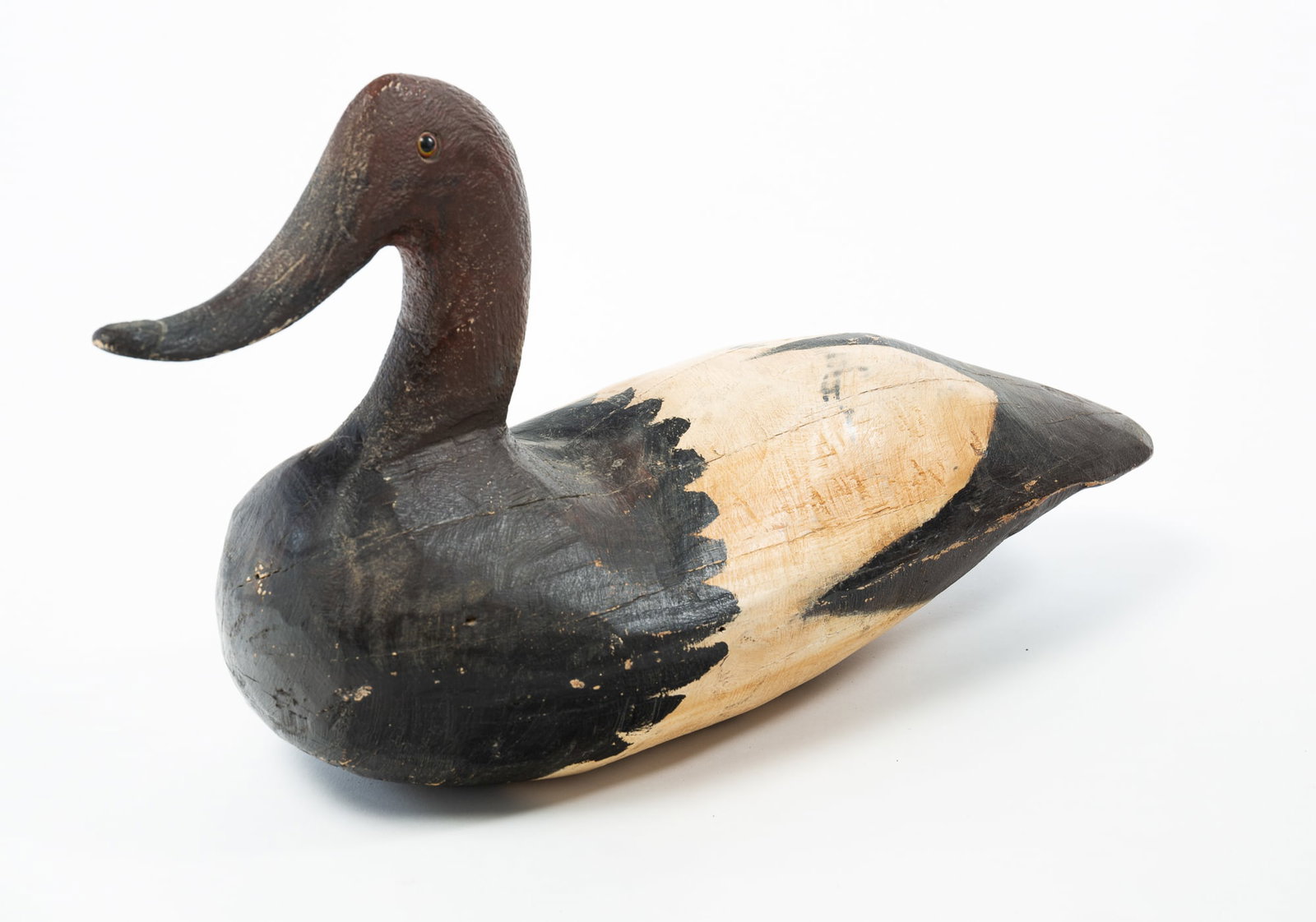 LARGE CARVED AND PAINTED CANVASBACK DUCK DECOY.: LARGE CARVED AND PAINTED CANVASBACK DUCK DECOY. American, 20th Century. Wood. In shades of red, black, and cream. Having a high head with glass eyes and a curved, upturned bill continuing to a long bo