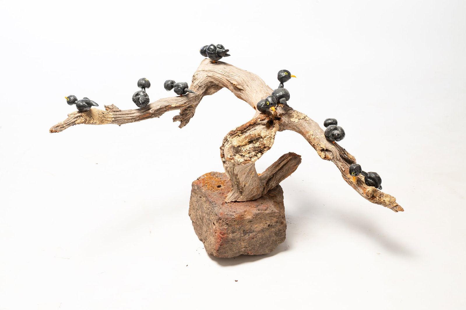 FOLK ART SCULPTURE OF CARVED AND PAINTED BLACK BIRDS ON A DRIFTWOOD BRANCH.: FOLK ART SCULPTURE OF CARVED AND PAINTED BLACK BIRDS ON A DRIFTWOOD BRANCH. American, 20th Century. Eight carved and painted wooden black birds perched on a driftwood branch bolted to a heavy
