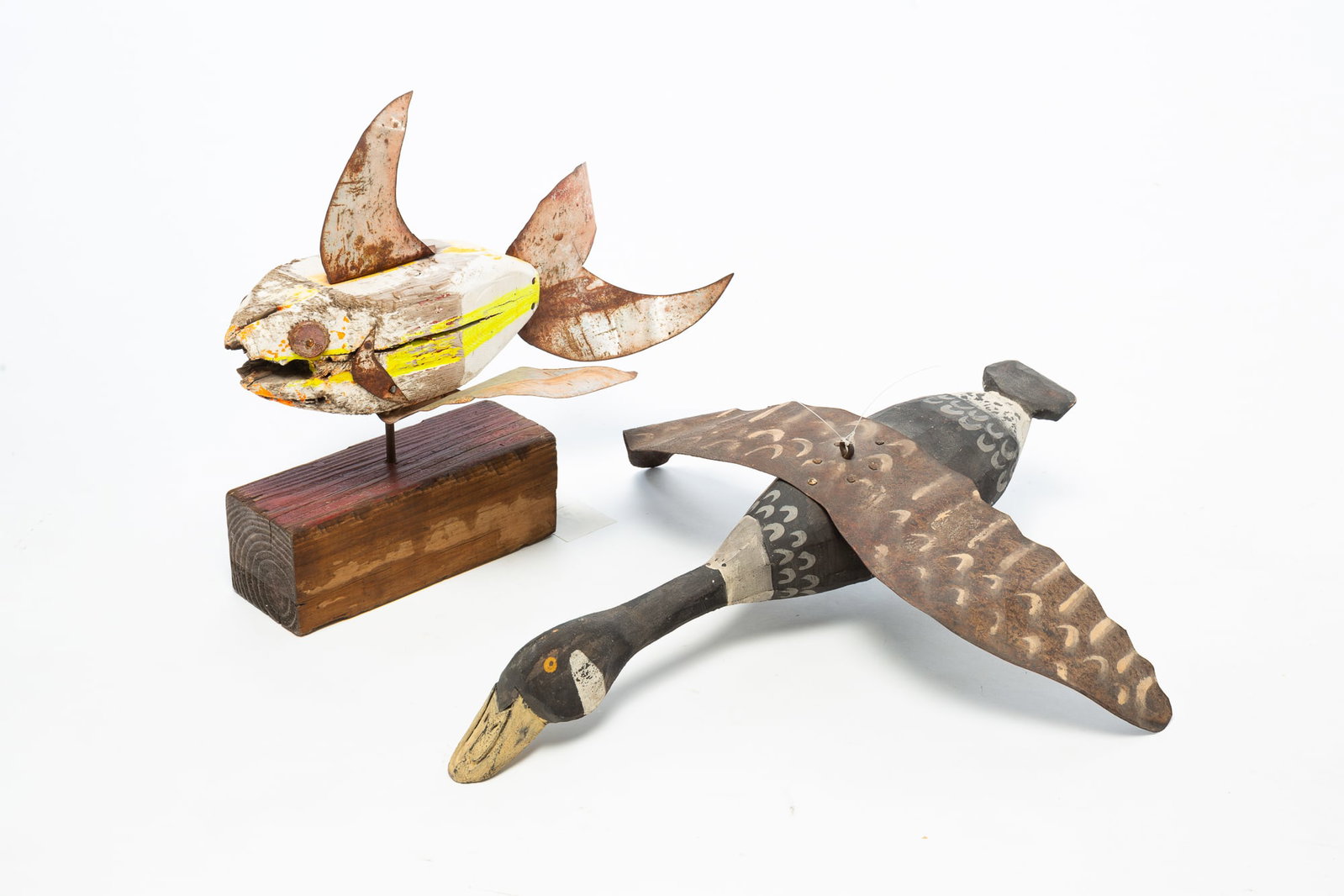 TWO FOLKSY CARVINGS WITH SHEET METAL ACCENTS.: TWO FOLKSY CARVINGS WITH SHEET METAL ACCENTS. American, 20th Century. A fish carving with vibrant paint, bottlecap eyes, and rust patina, mounted on a wood base, 15"h. Accompanied by a goose carved de